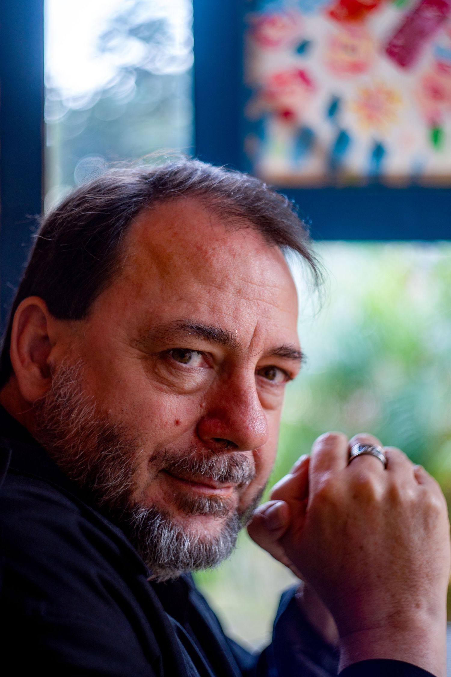 Portrait of person in black shirt with grey beard resting chin on hand.