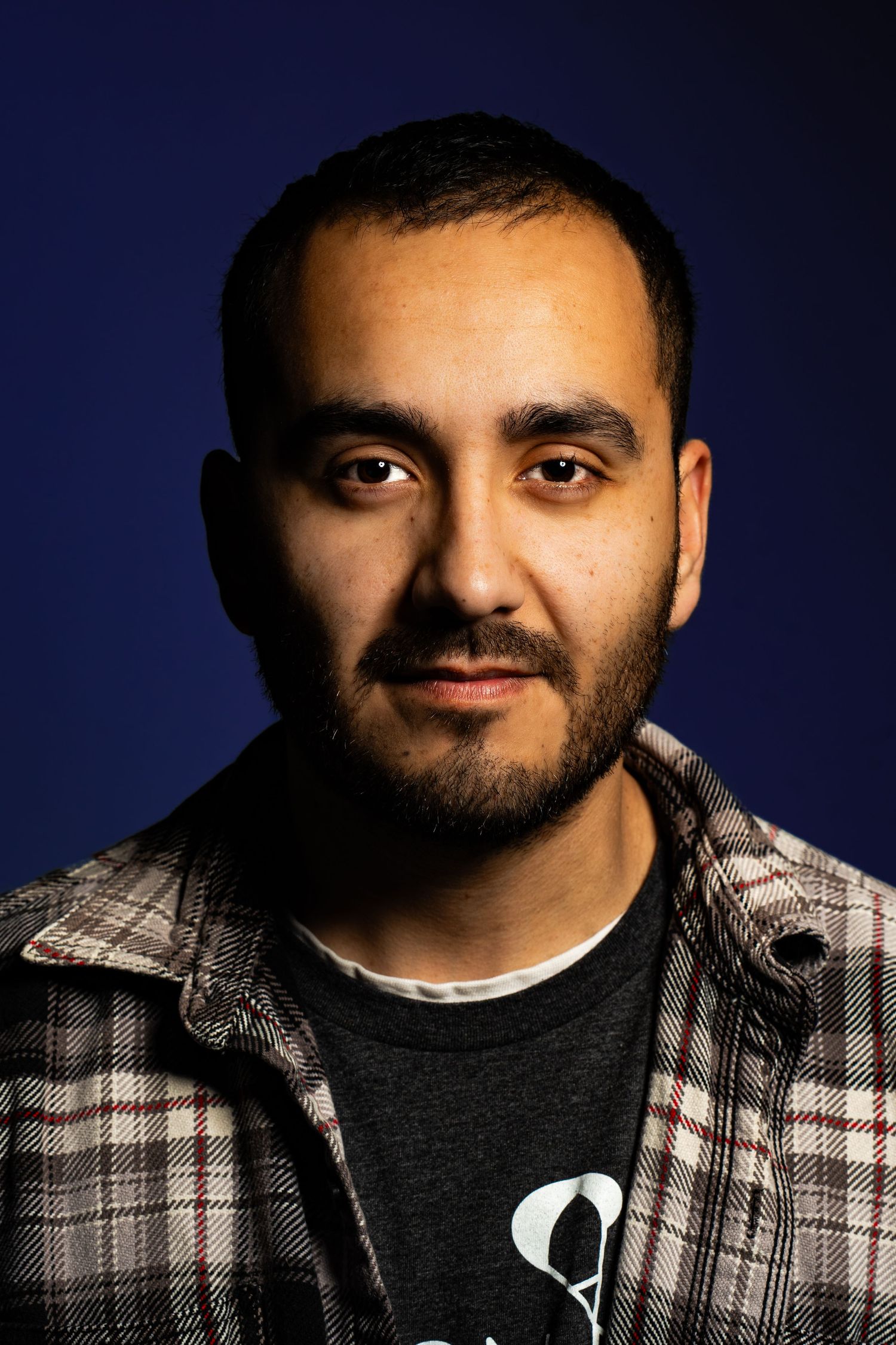 Portrait of person in plaid shirt against dark blue background.