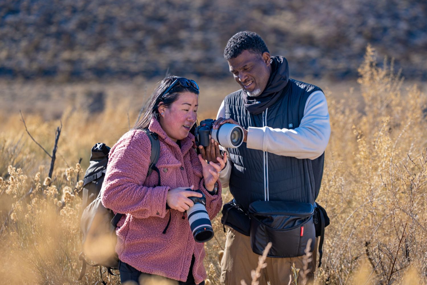 Two photographers reviewing photos on a camera in an outdoor setting.