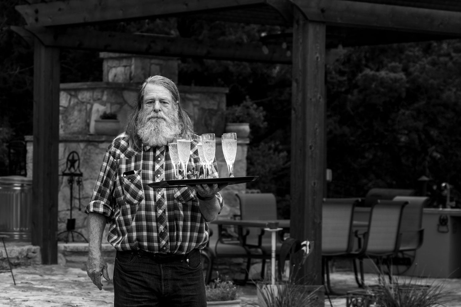 Black and white portrait of a bearded man in plaid shirt standing outdoors.