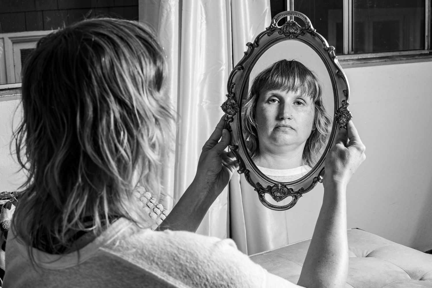 Black and white photo of someone looking at their reflection in an ornate mirror.