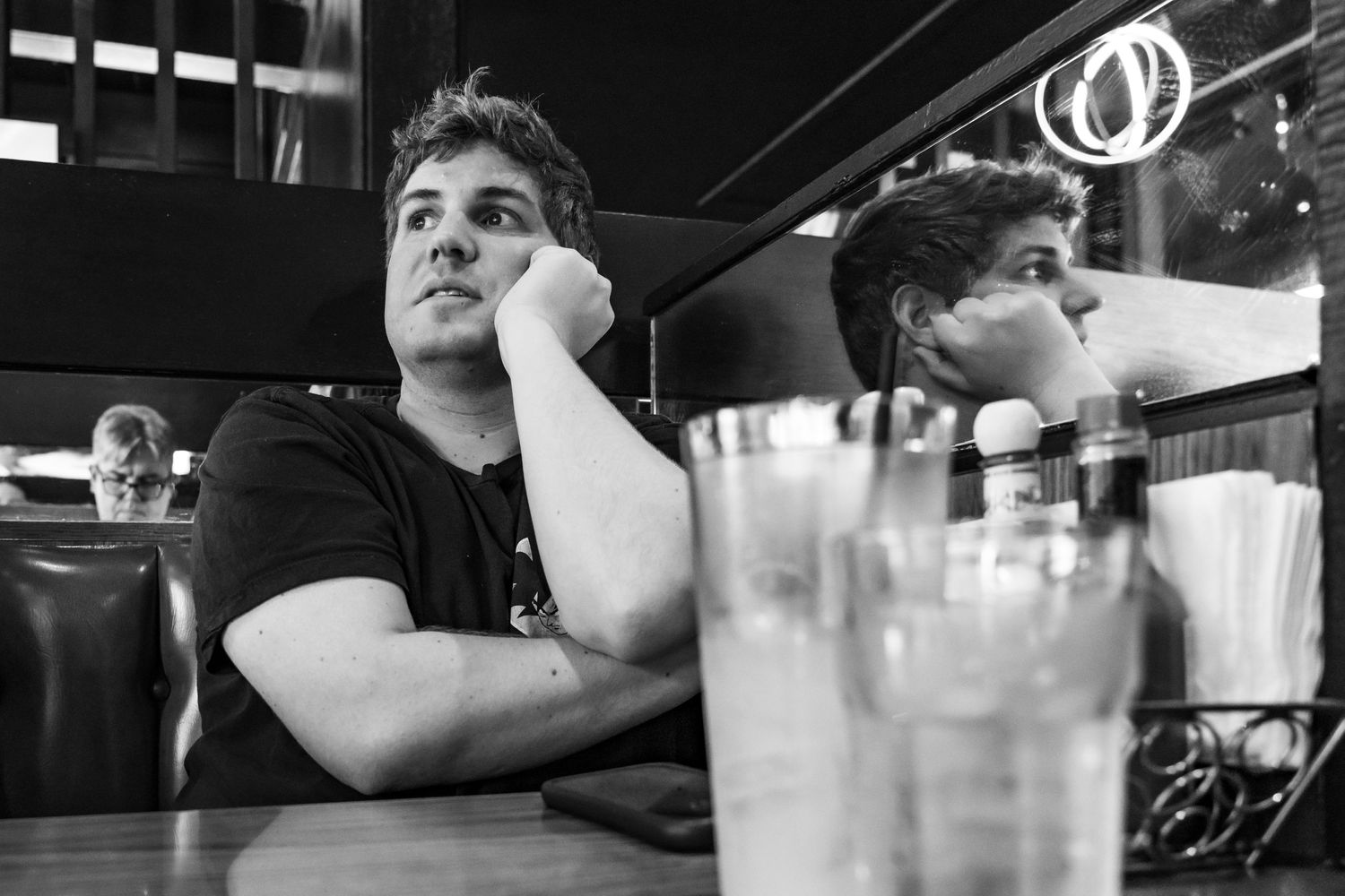 A contemplative scene in black and white showing a person sitting at a counter in a dimly lit diner.