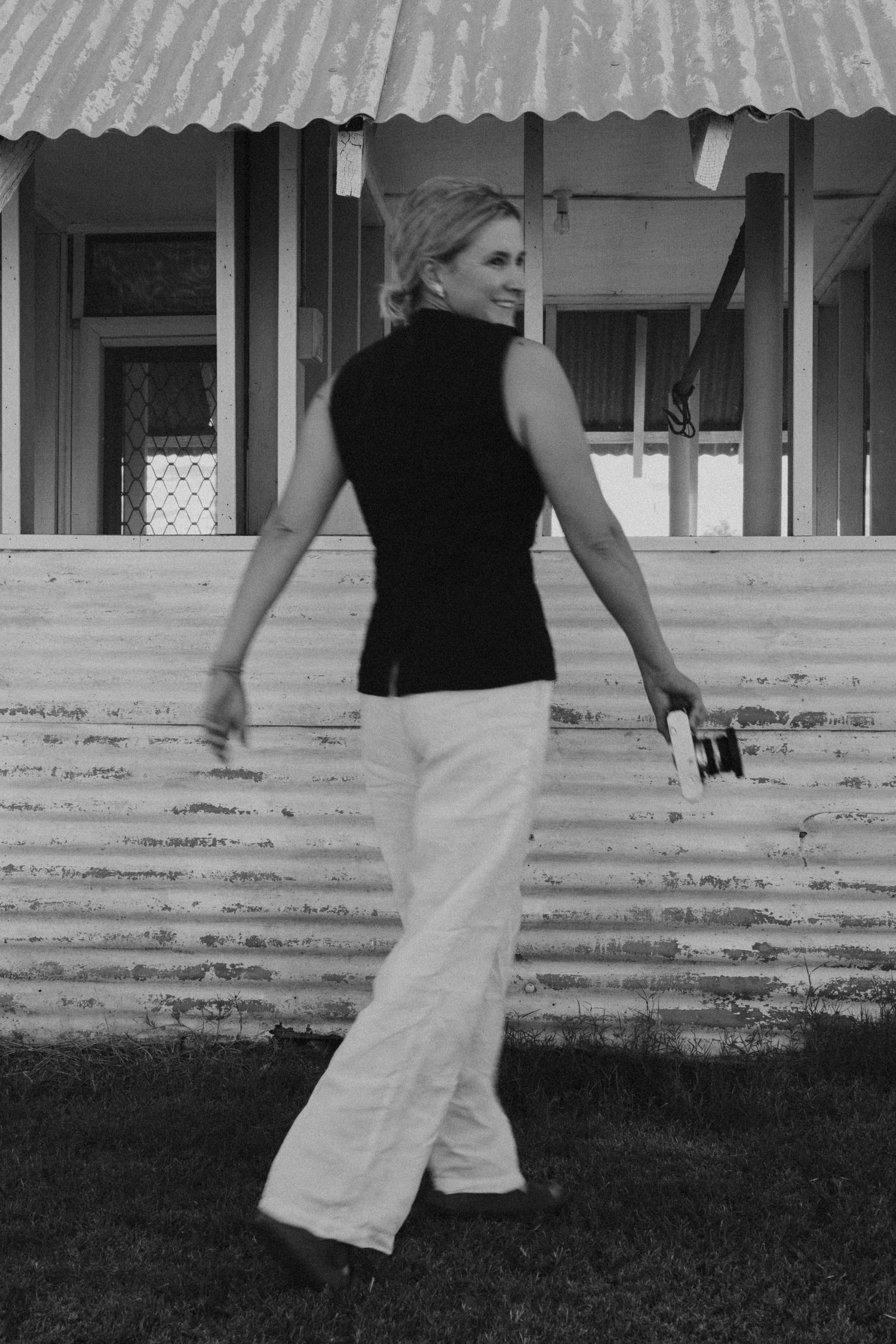Person in black sleeveless top and white pants standing outside a building.