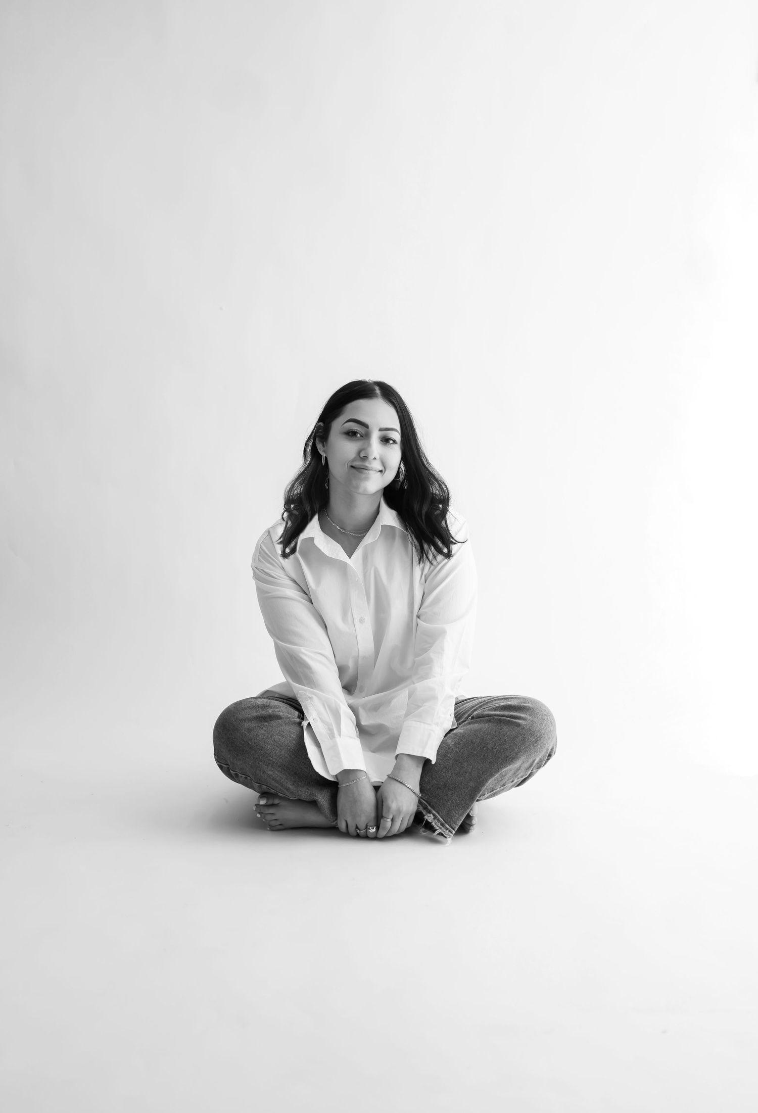 Minimalist portrait of a person sitting cross-legged in white shirt against white background.