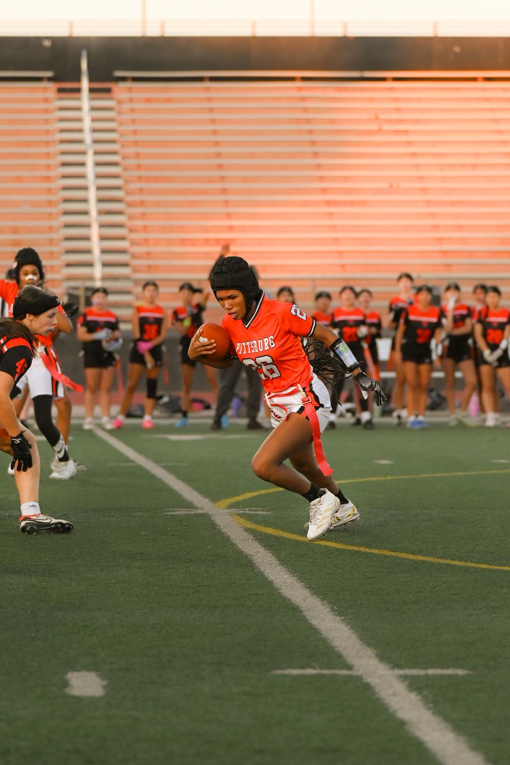 Player in orange jersey runs with football during sunset game.