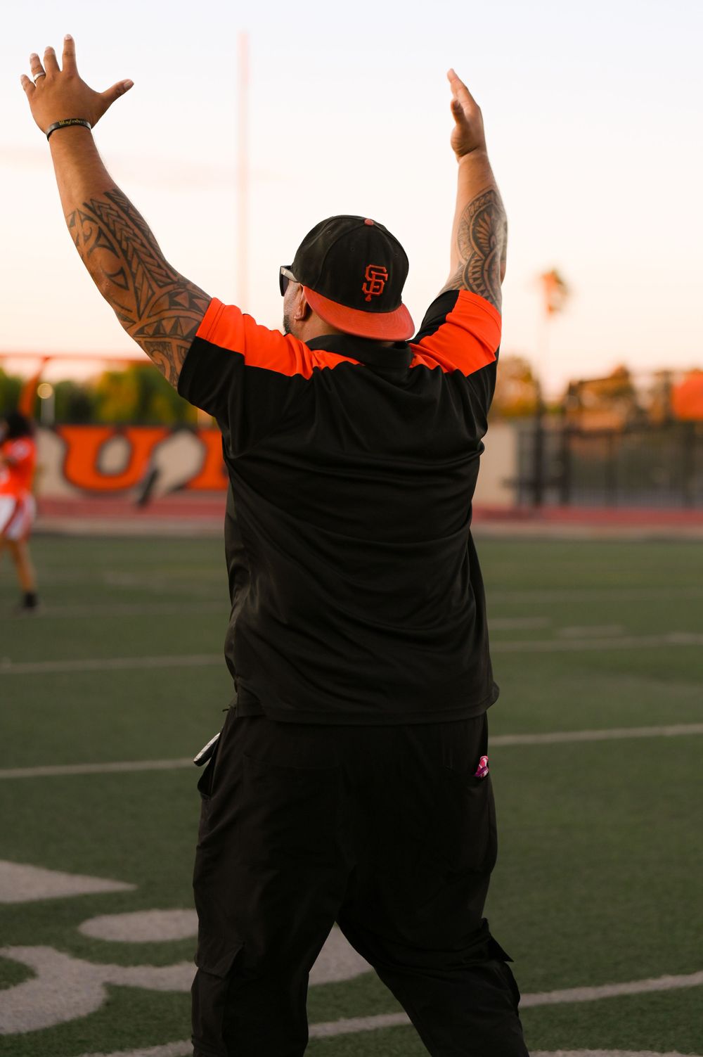 Coach raises arms in celebration wearing black outfit and SF Giants cap.