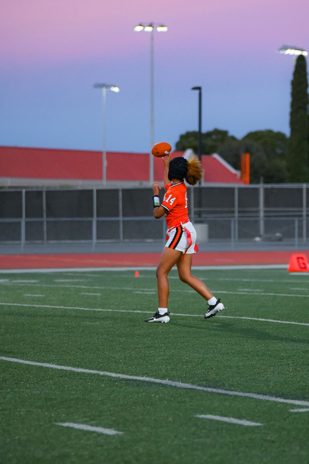 Athlete in orange uniform practices throwing drills during sunset.