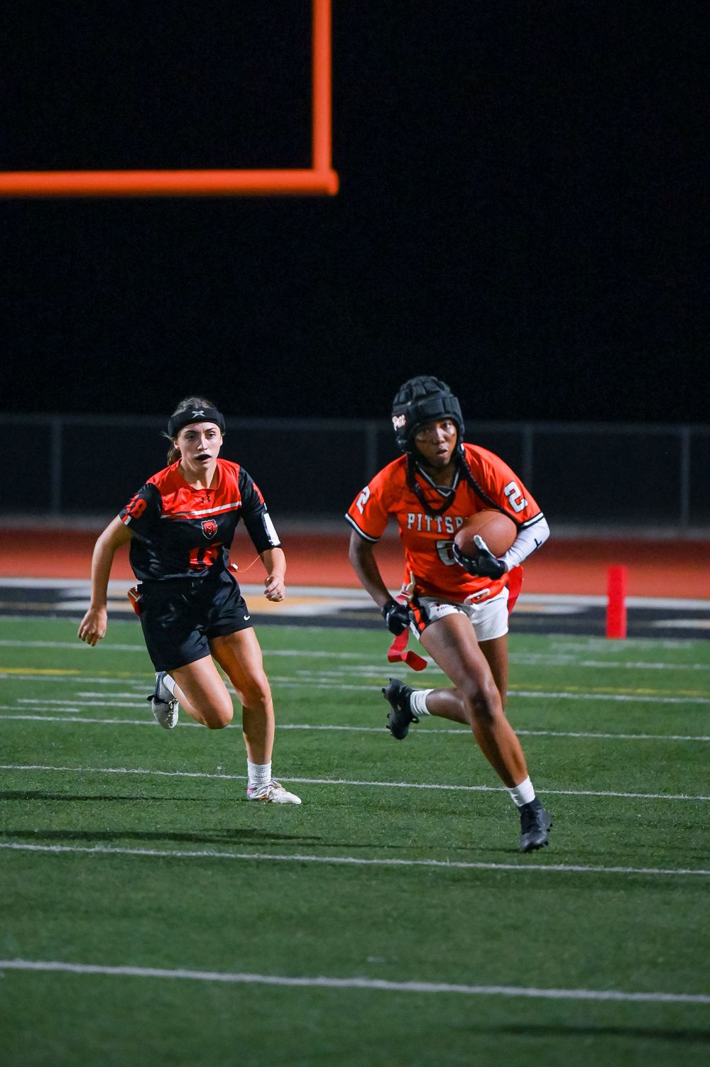Two players sprint across football field during nighttime game.