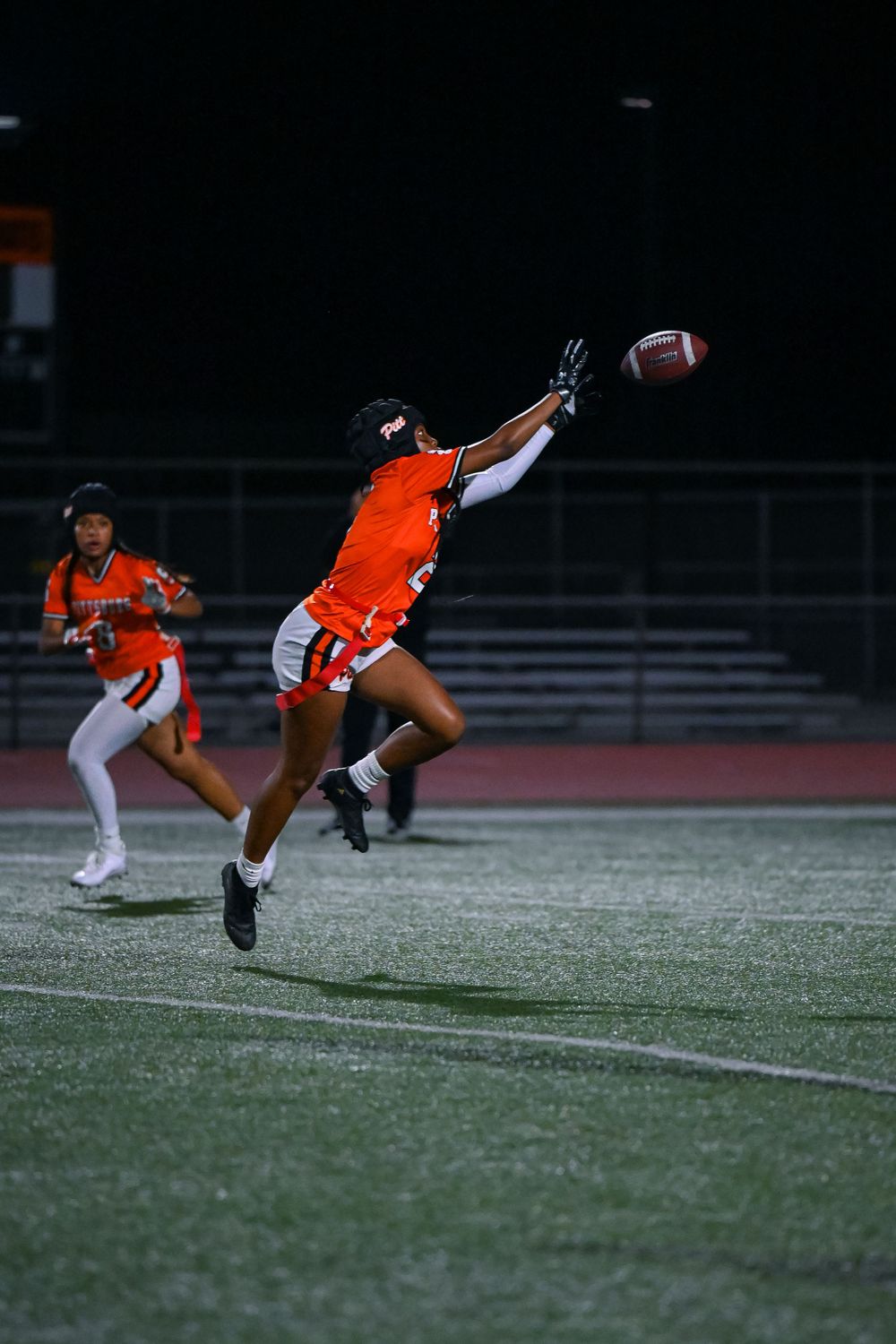 Football player in orange uniform makes a diving catch attempt during a nighttime game.
