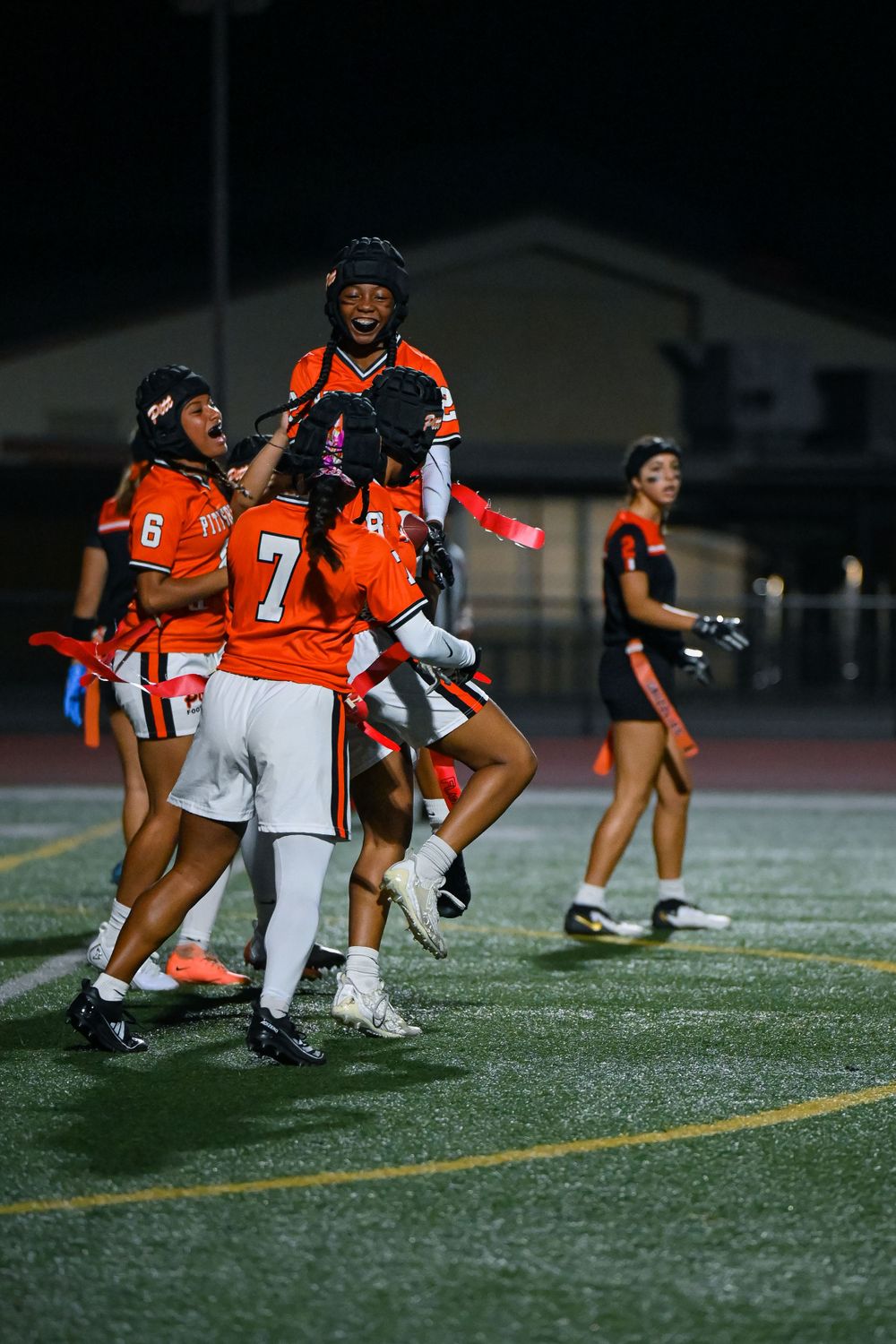 Players in orange uniforms practicing drills on a football field at night.
