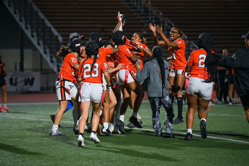 Football team celebrates together on the sidelines during a night game.