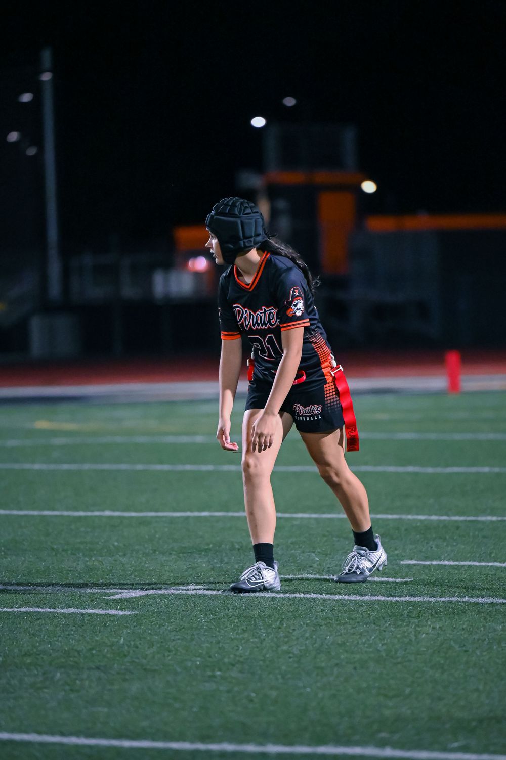 Player in black uniform crouches in ready position on the football field.