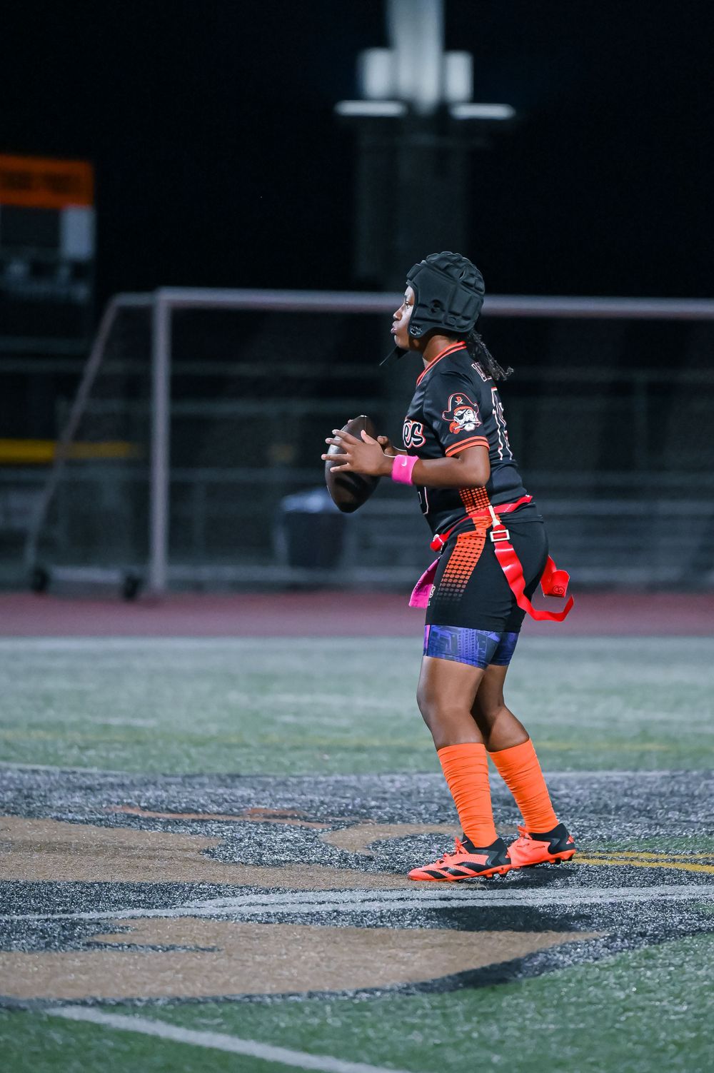 Player in orange and black uniform prepares for play on the football field at night.