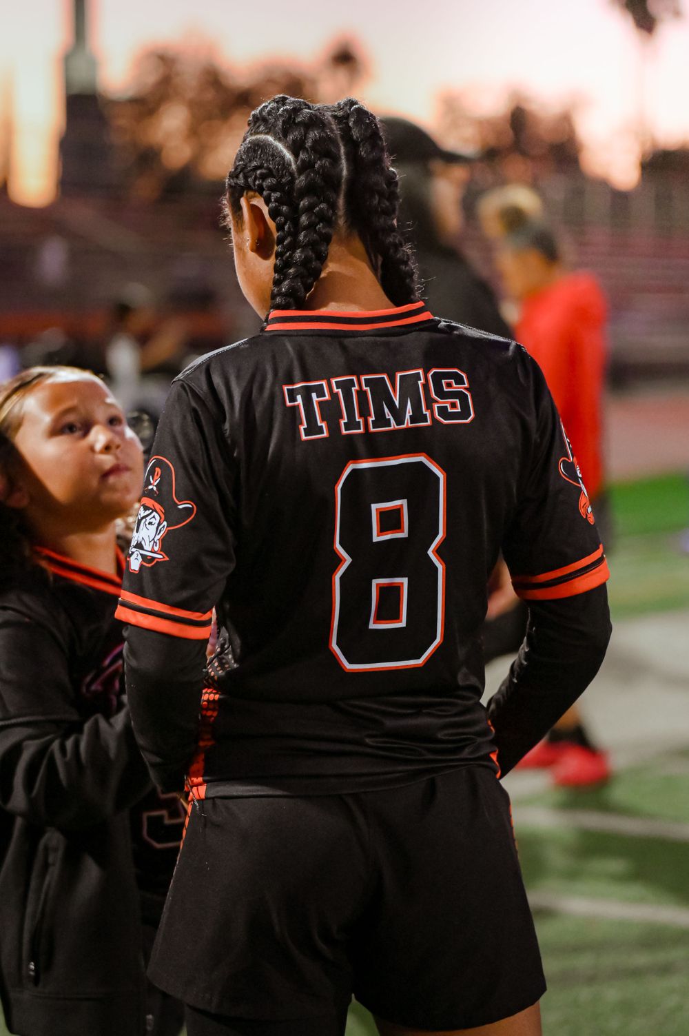 Back view of football players wearing black jerseys with numbers during a game.