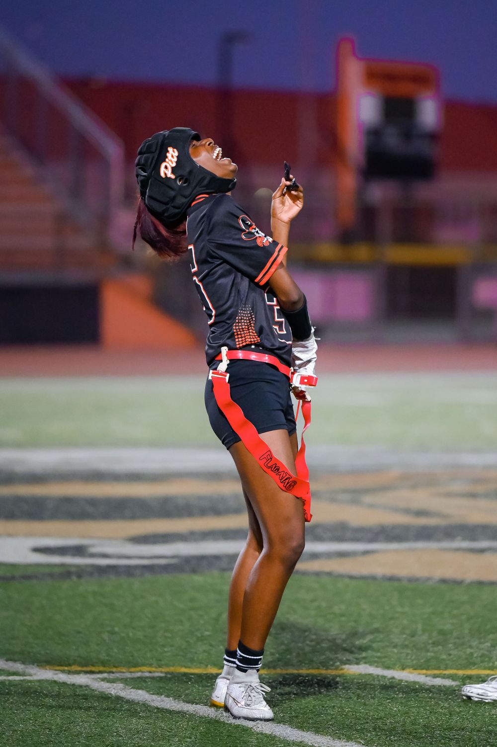 Player in black uniform performs stretching exercises on the football field.