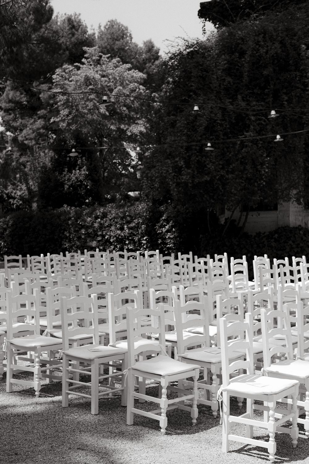 Rows of white wooden chairs set up for an outdoor ceremony under string lights.