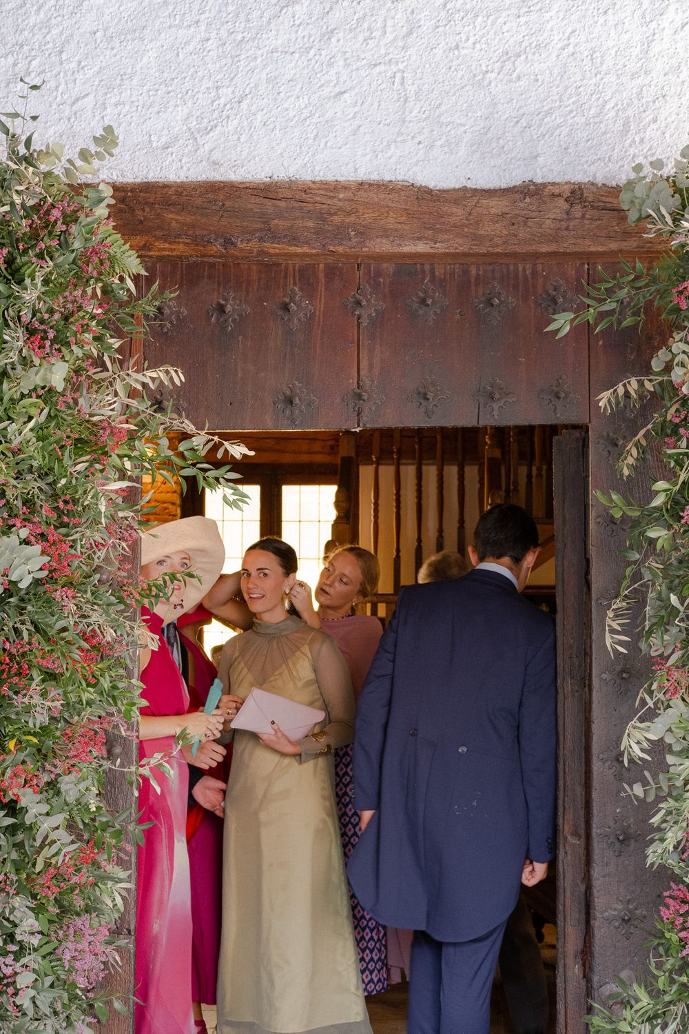 Wedding guests gathered at rustic wooden doorway decorated with climbing roses and greenery.