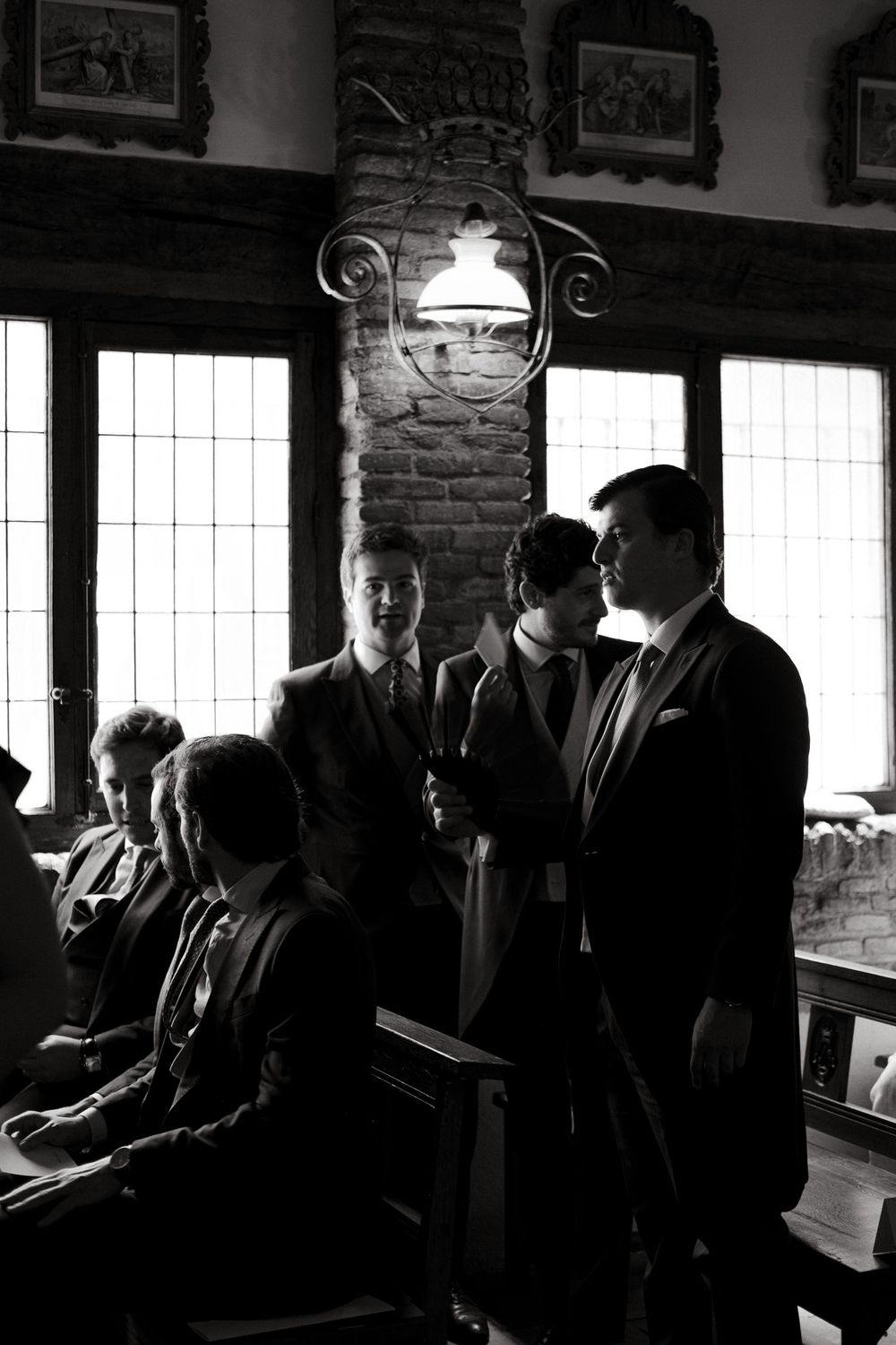 Black and white photo of gathering in historic room with exposed brick and vintage lighting.
