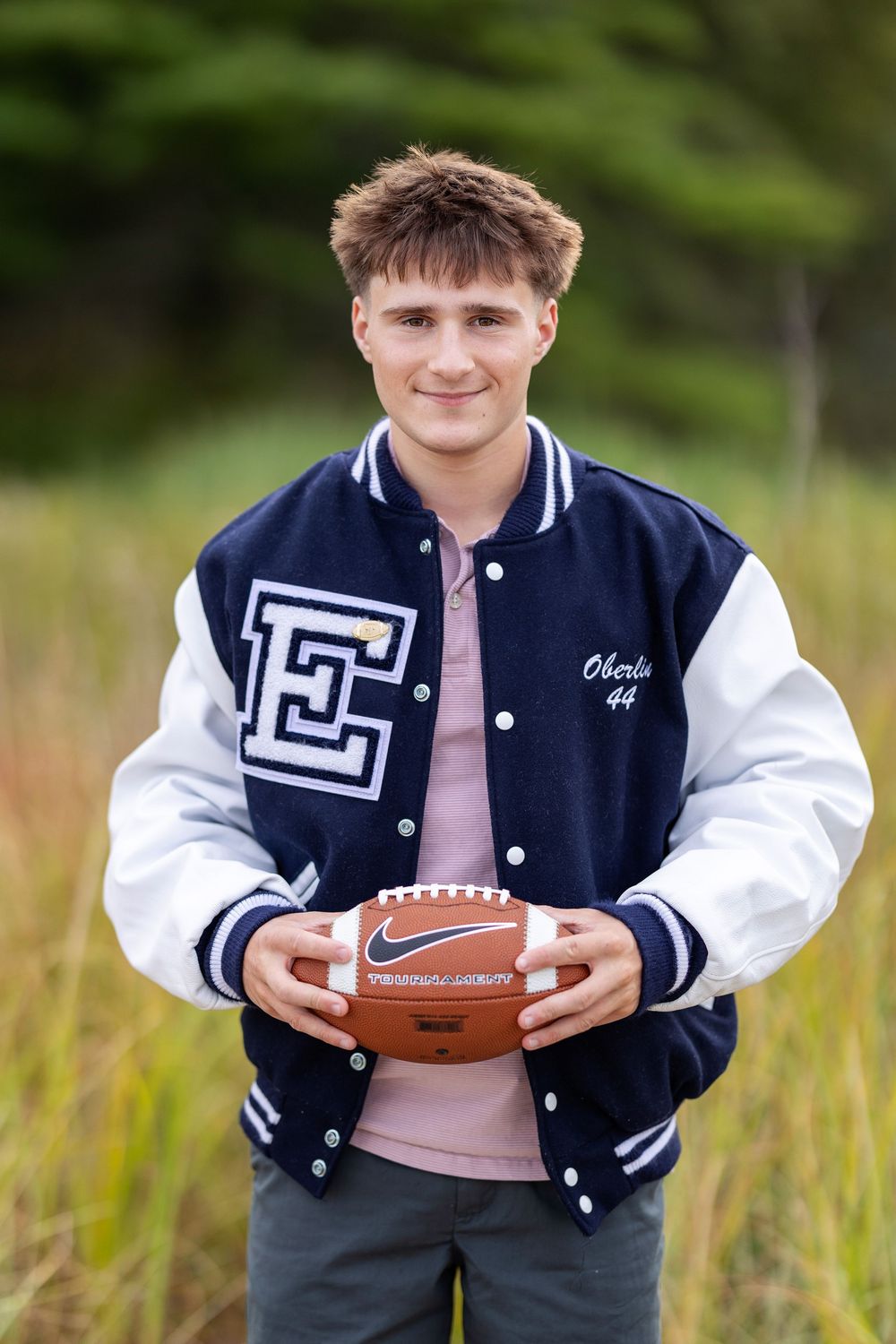 High school senior portrait wearing football jacket and holding football in field at New Castle NH
