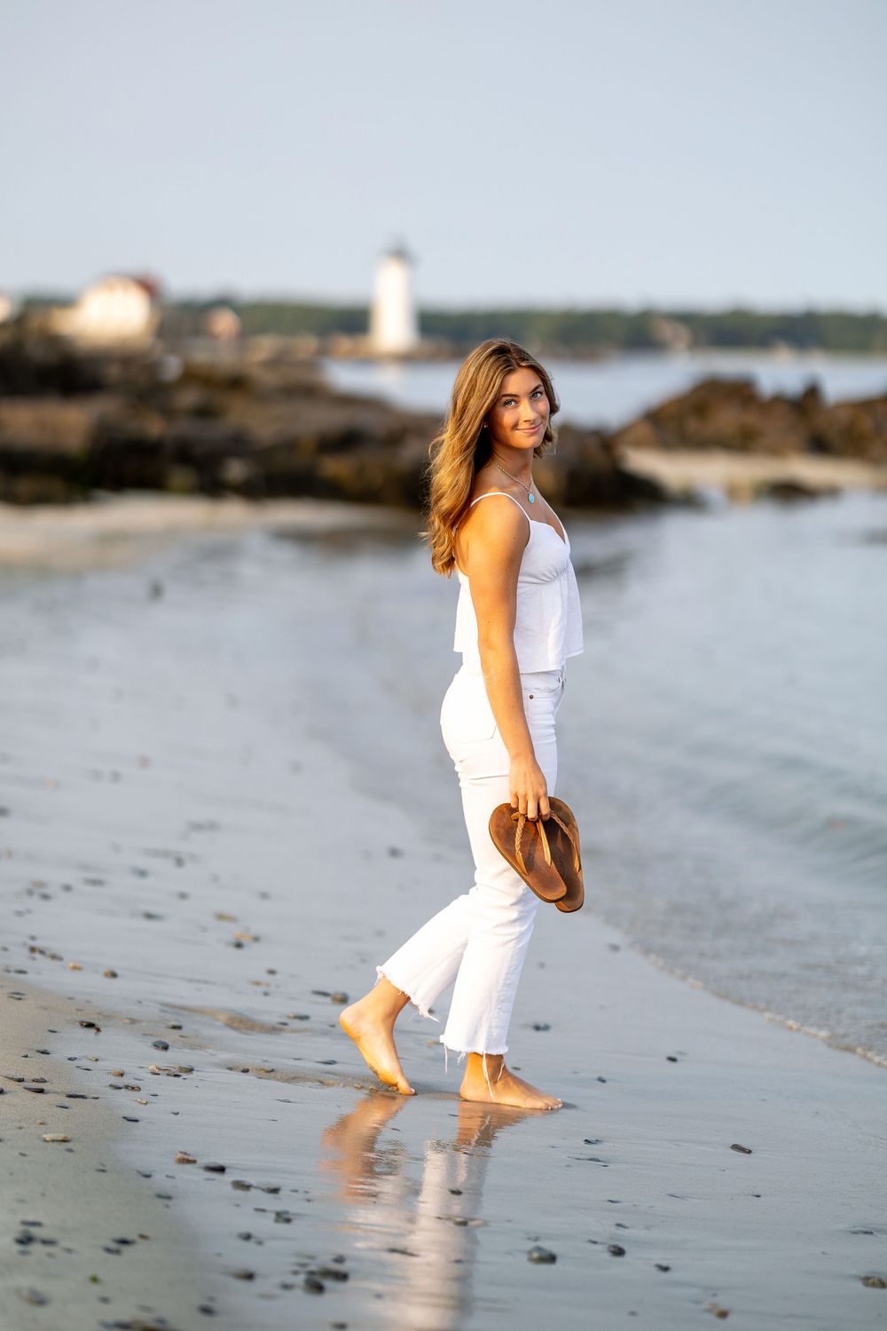 High school senior portrait at sunset at the beach New Castle, NH with water, sand, rocks and lighthouse