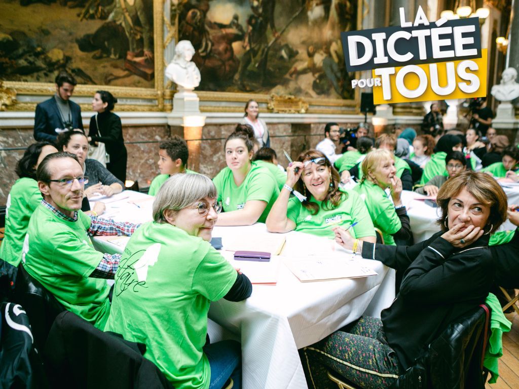 Group of people in bright green shirts seated at tables during what appears to be a formal event or competition.