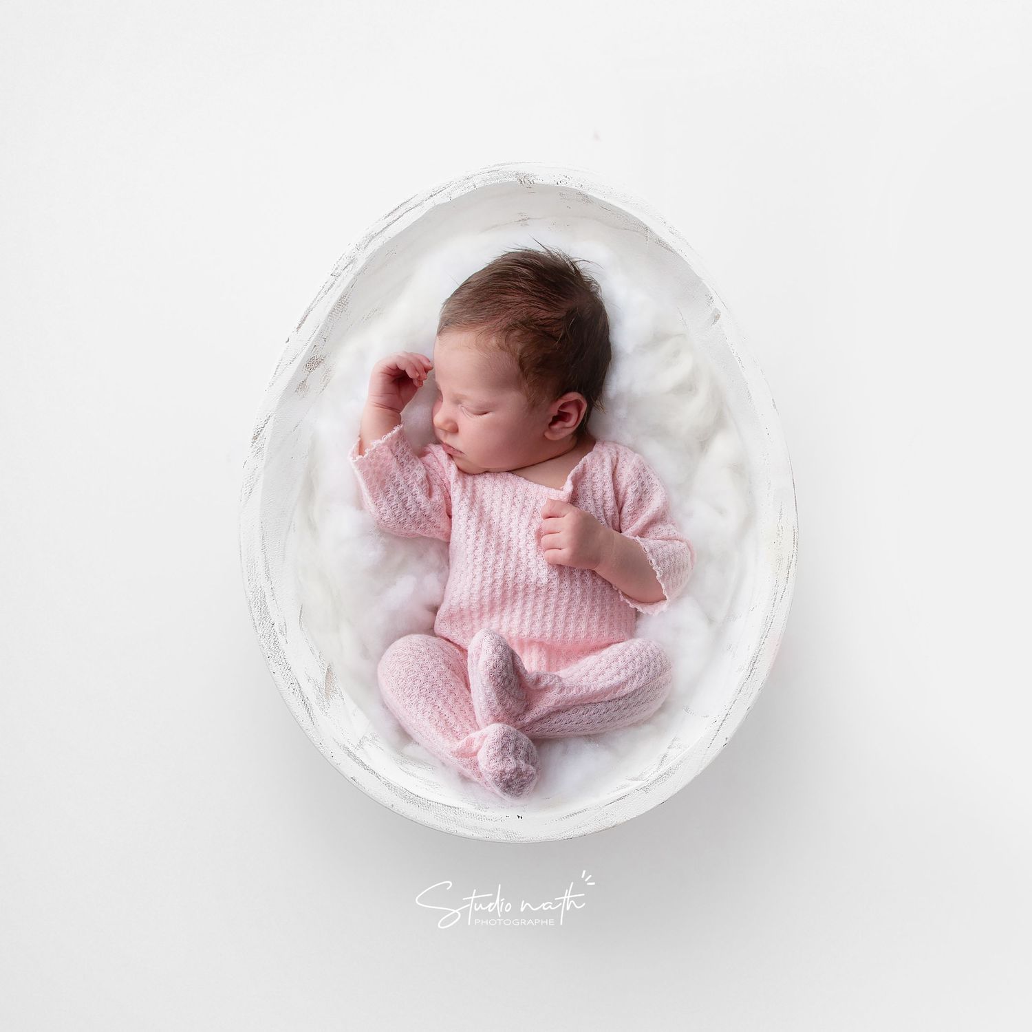 Sleeping newborn in pink striped outfit nestled in white bowl.