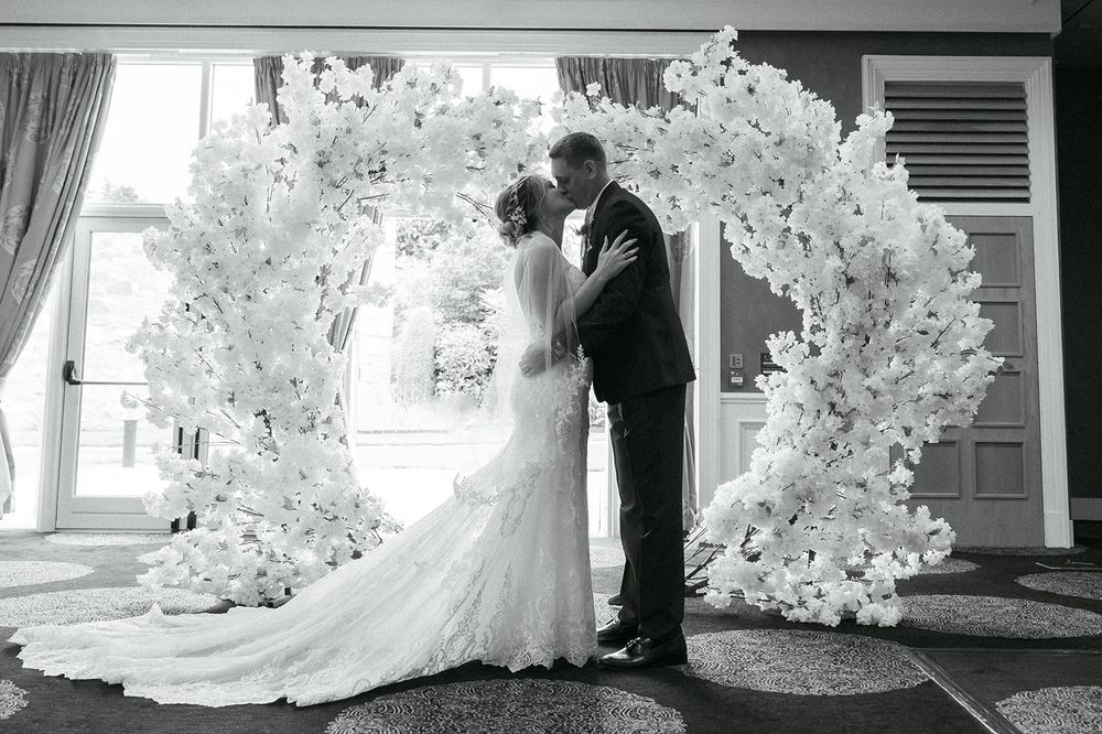 Dramatic silhouettes of a wedding couple against white floral decorations.