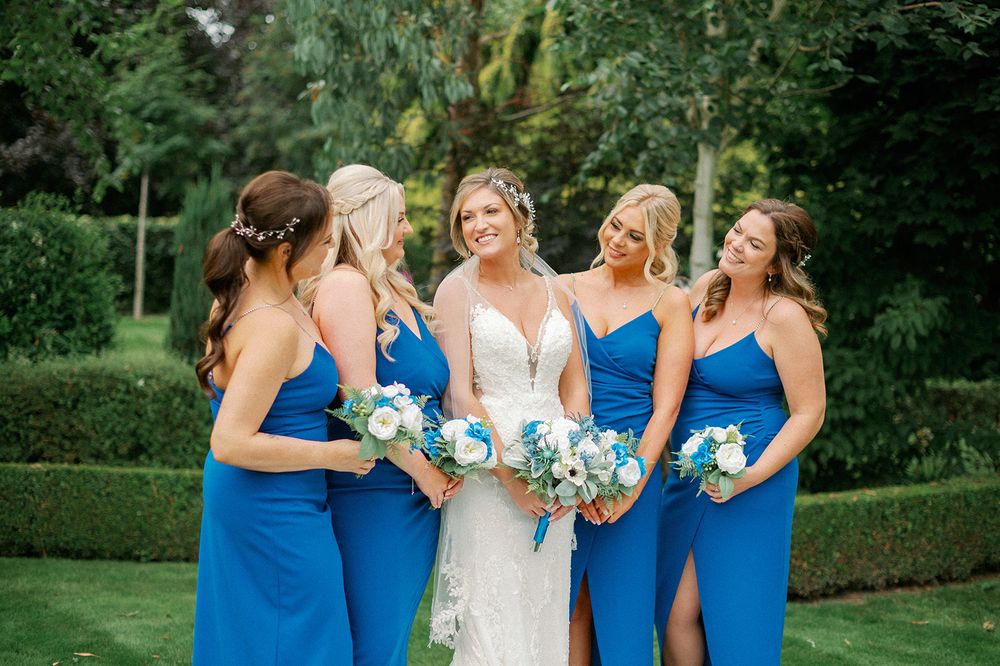 Wedding party in bright blue bridesmaid dresses holding bouquets in a garden setting.