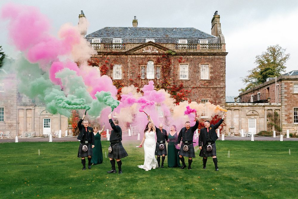 Pink smoke bombs create dramatic effect against historic Culloden House during wedding photo session.