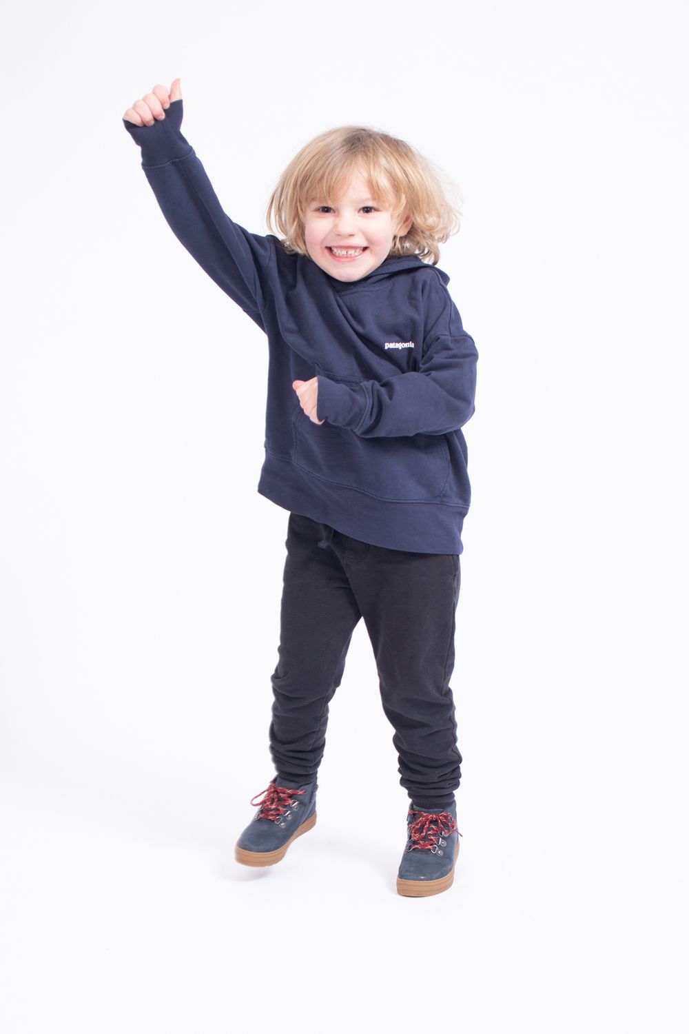 Energetic toddler in navy hoodie and black pants jumping with raised arm.