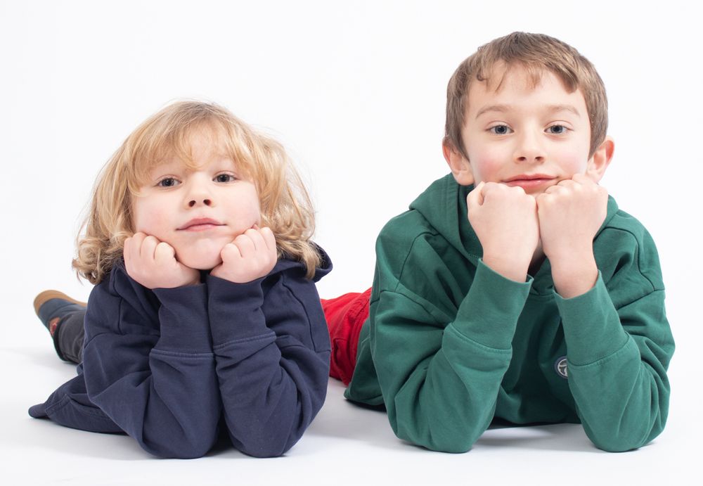Two children lying on floor with chins resting on hands against white background.