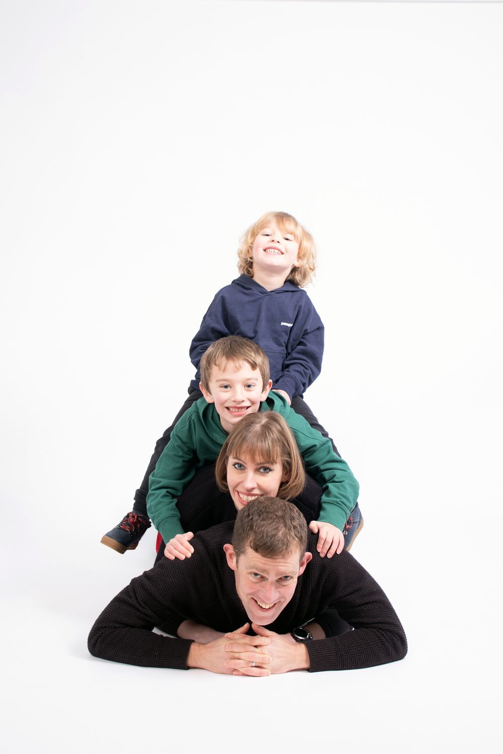 Four people stacked on top of each other in playful pyramid pose against white background.