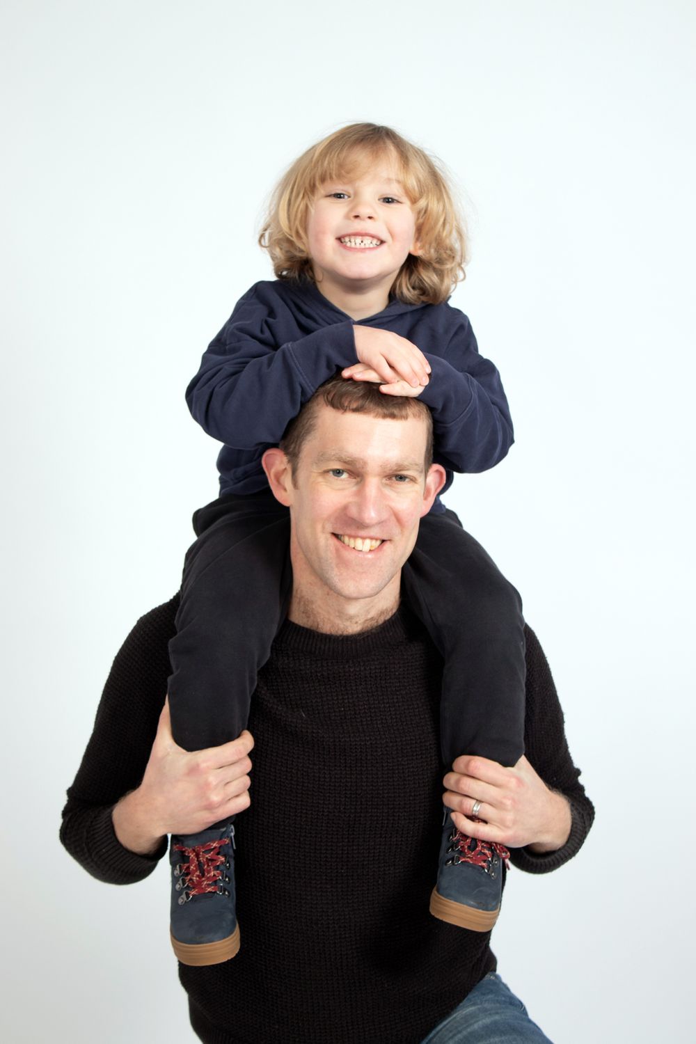 Parent giving child shoulder ride against white background wearing matching dark sweaters.