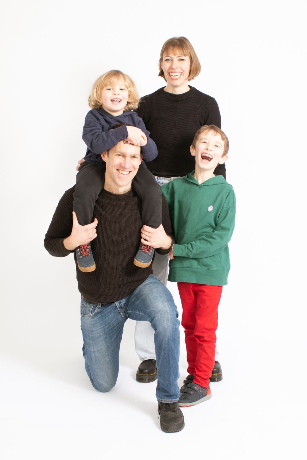 Family portrait with parents and children smiling against white background in casual attire.