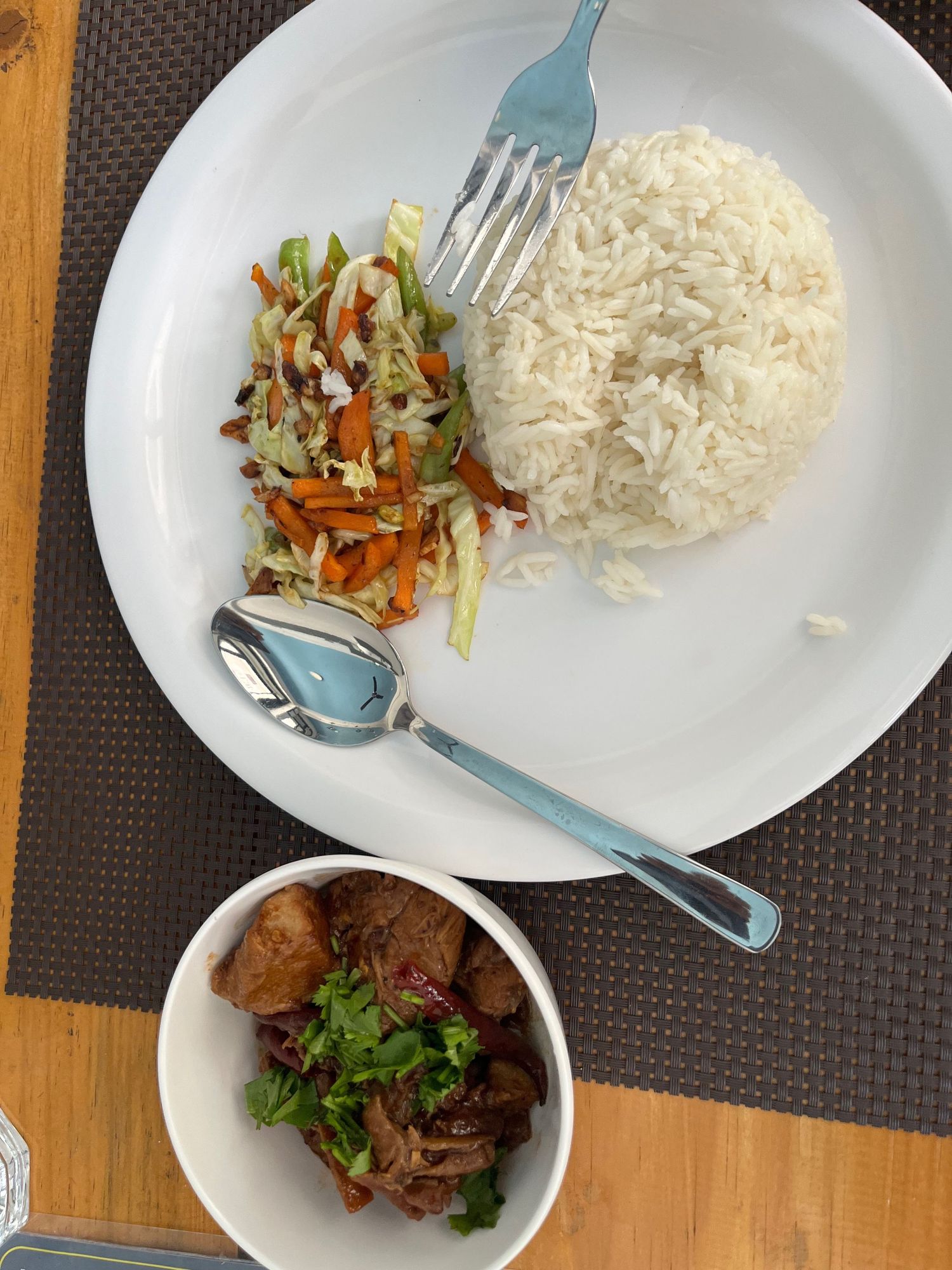 White plates with steamed rice and meat dishes served on a dark woven placemat.