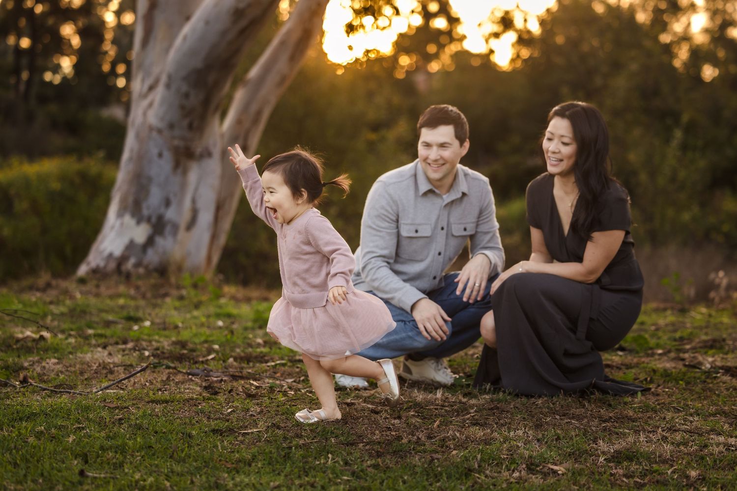 A candid family portrait taken at sunset under a large tree in a natural outdoor setting.