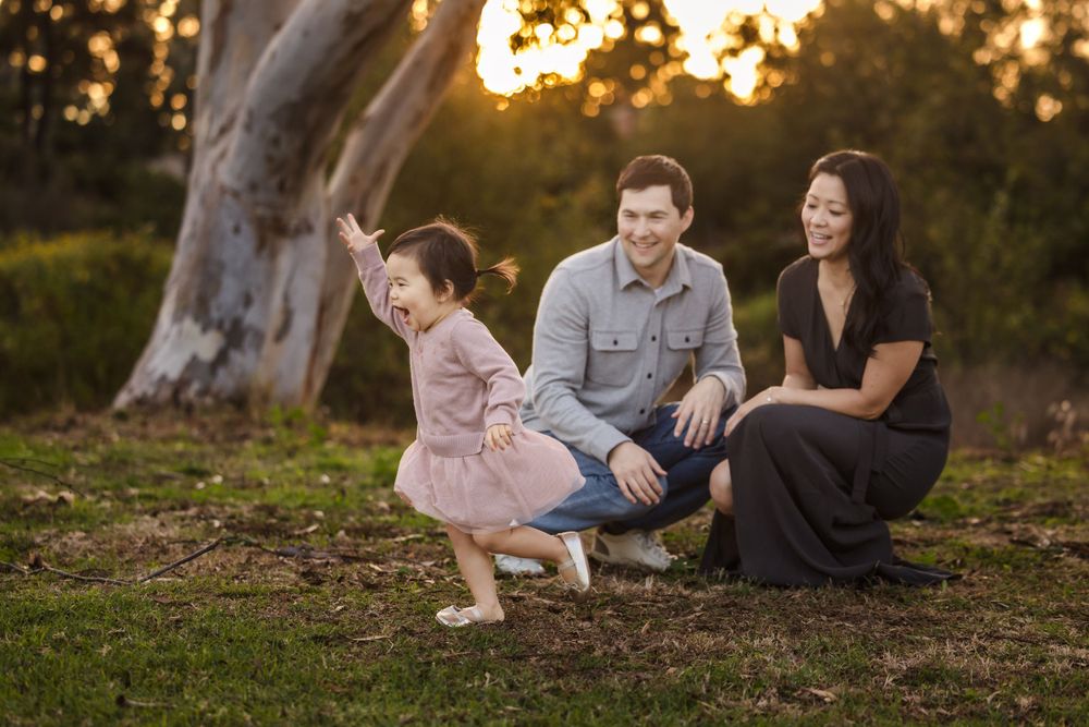 A candid family portrait taken at sunset under a large tree in a natural outdoor setting.