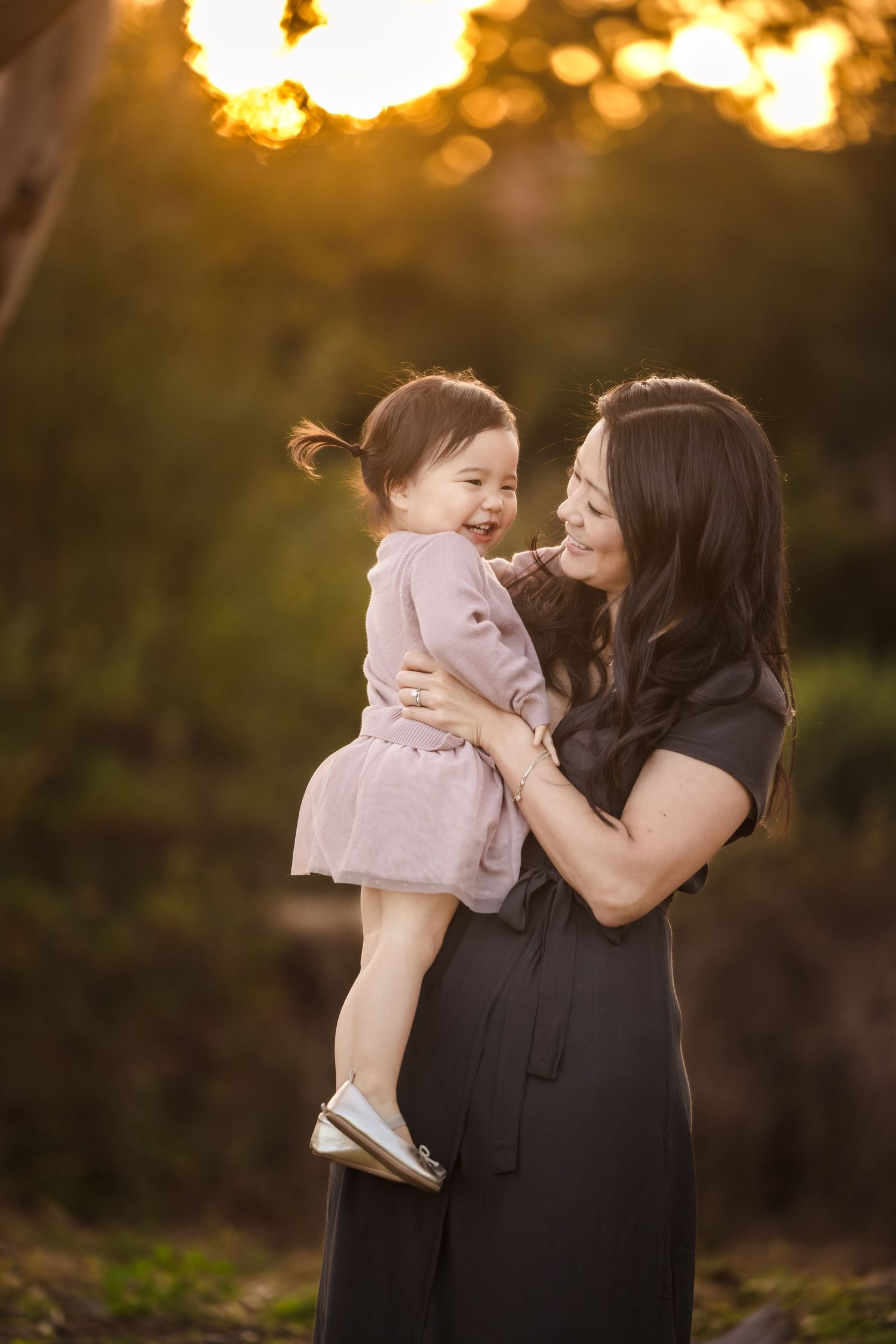 A mother and child share a joyful moment at sunset with golden bokeh lighting in the background.