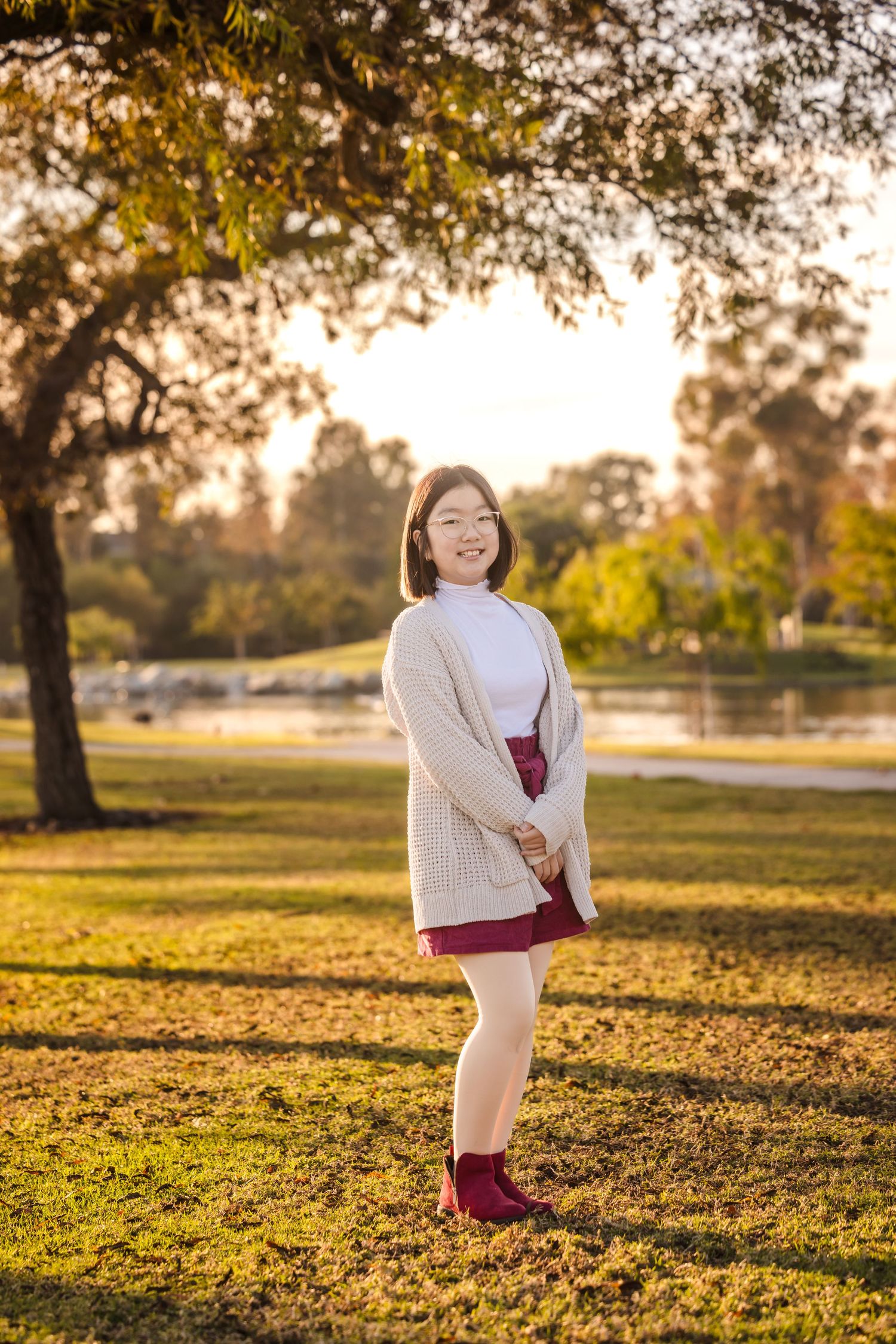 Person poses joyfully in a cozy sweater outfit at a park during sunset.