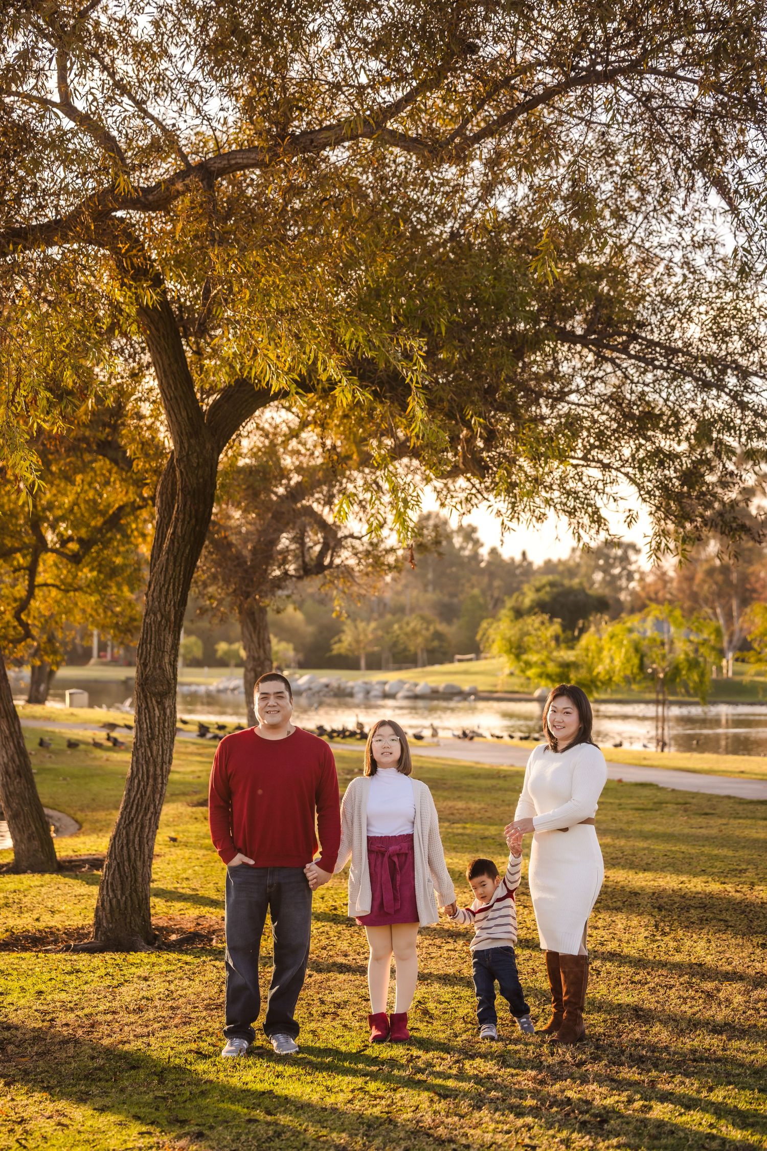 A family stands together under a golden autumn tree during sunset in a park with warm sunlight filtering through branches.