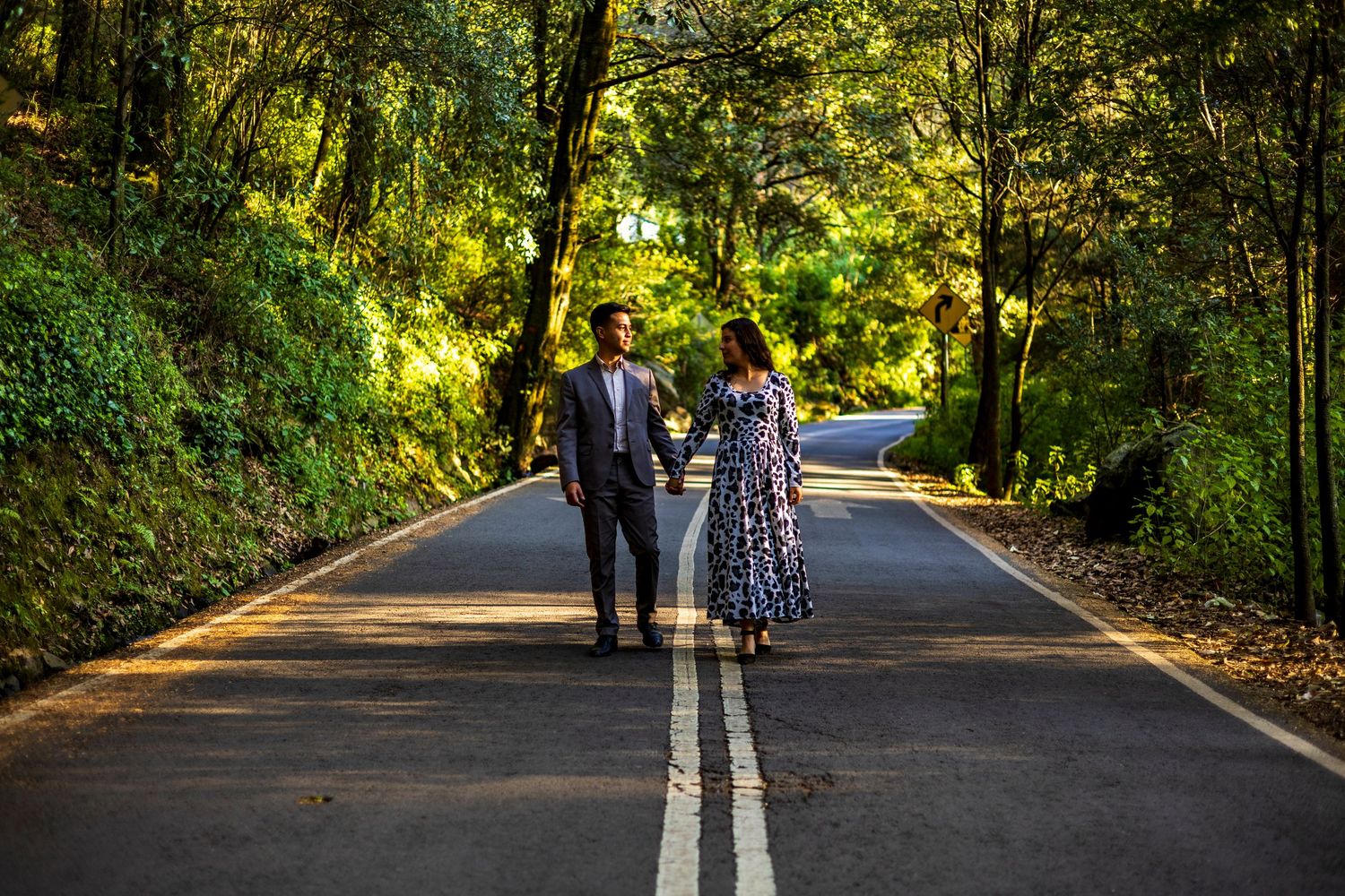 A couple walks down a tree-lined road surrounded by lush greenery.