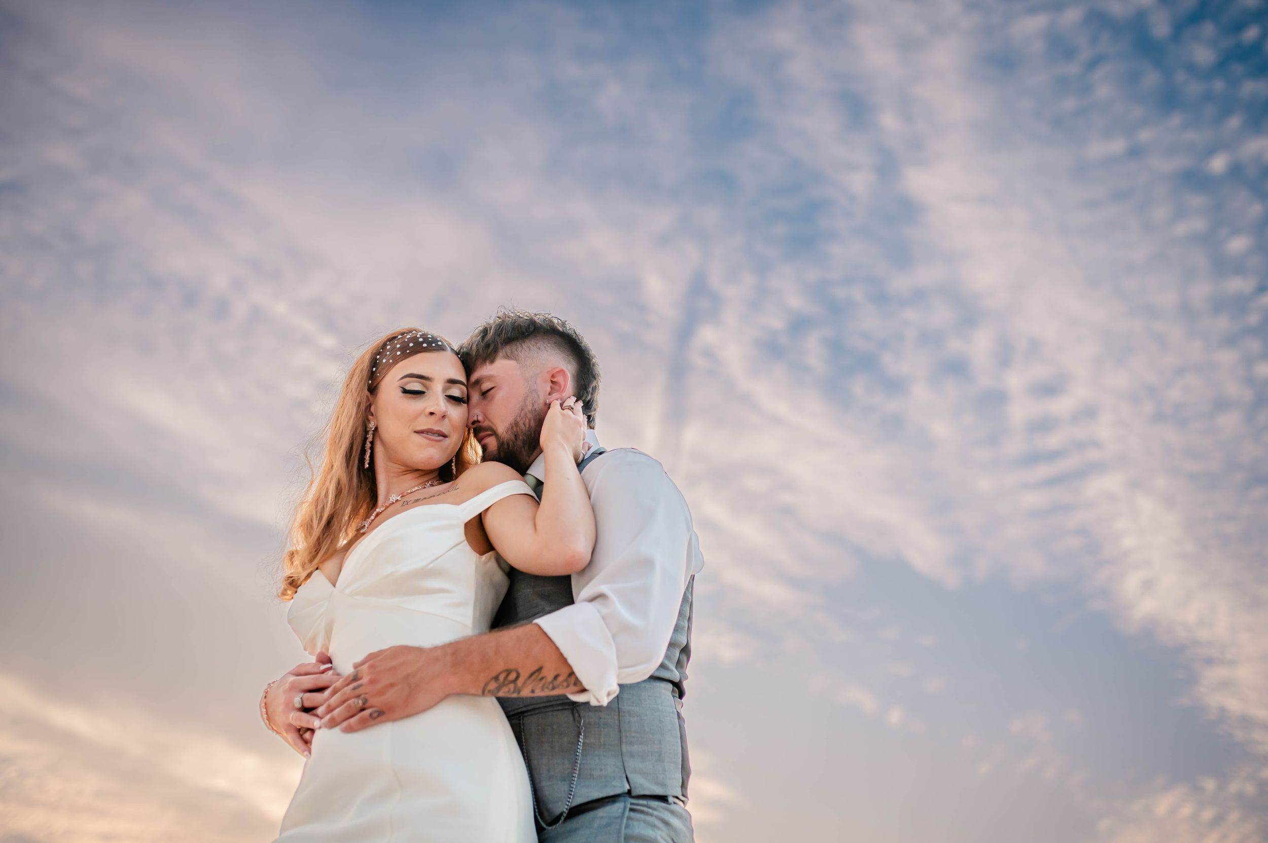 Romantic sunset portrait of newlyweds embracing against cloudy sky.