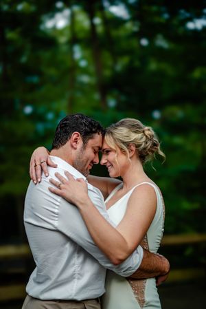 A romantic wedding couple shares an intimate moment outdoors with a soft green forest backdrop.