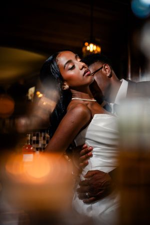 A romantic couple in elegant wedding attire share an intimate dance moment under warm lighting at their reception.