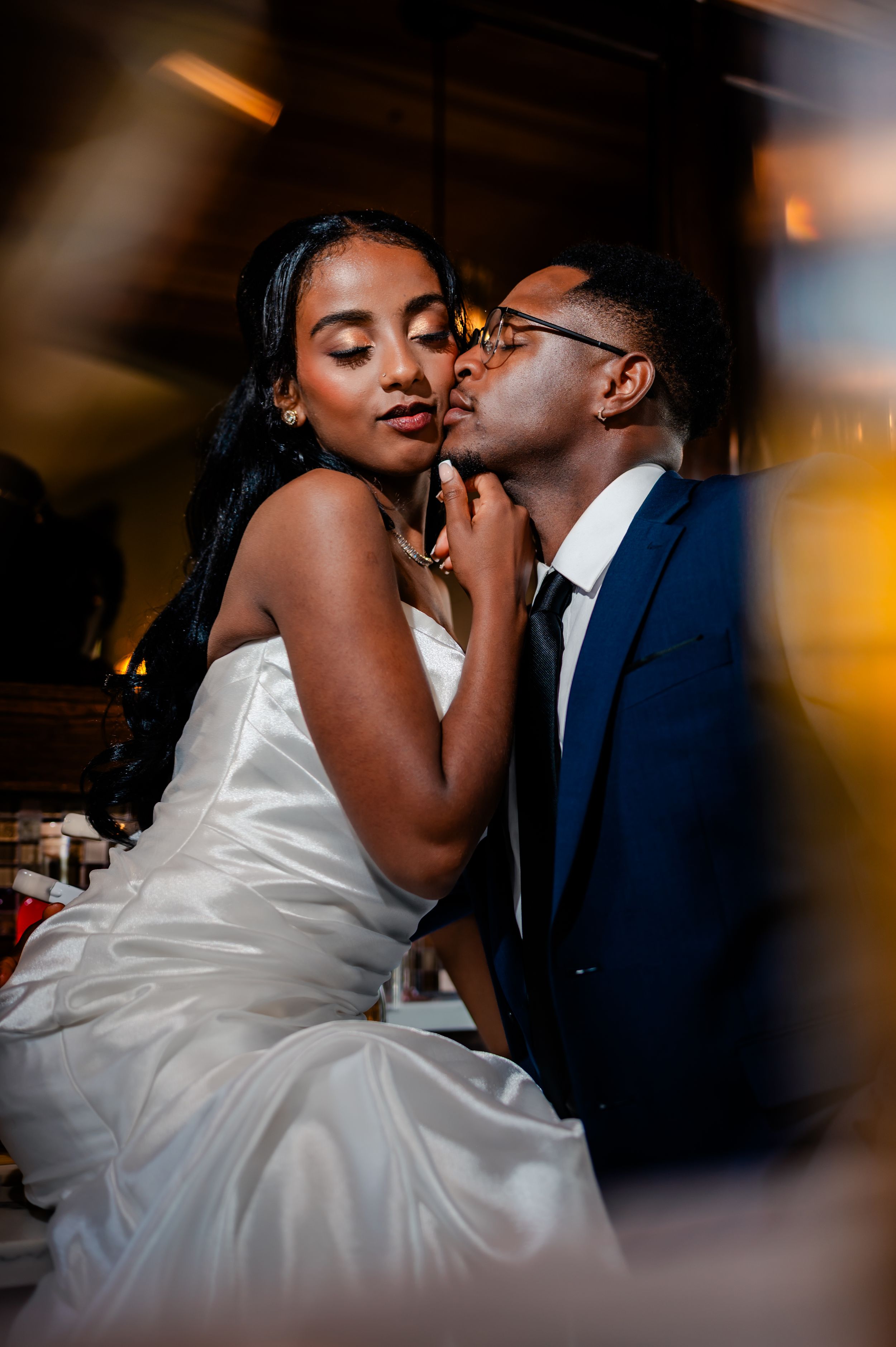 A romantic wedding moment captured in low light with the couple sharing an intimate embrace in formal attire.
