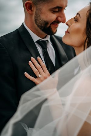 An intimate wedding portrait showing newlyweds in formal attire sharing a tender moment under a flowing white veil.