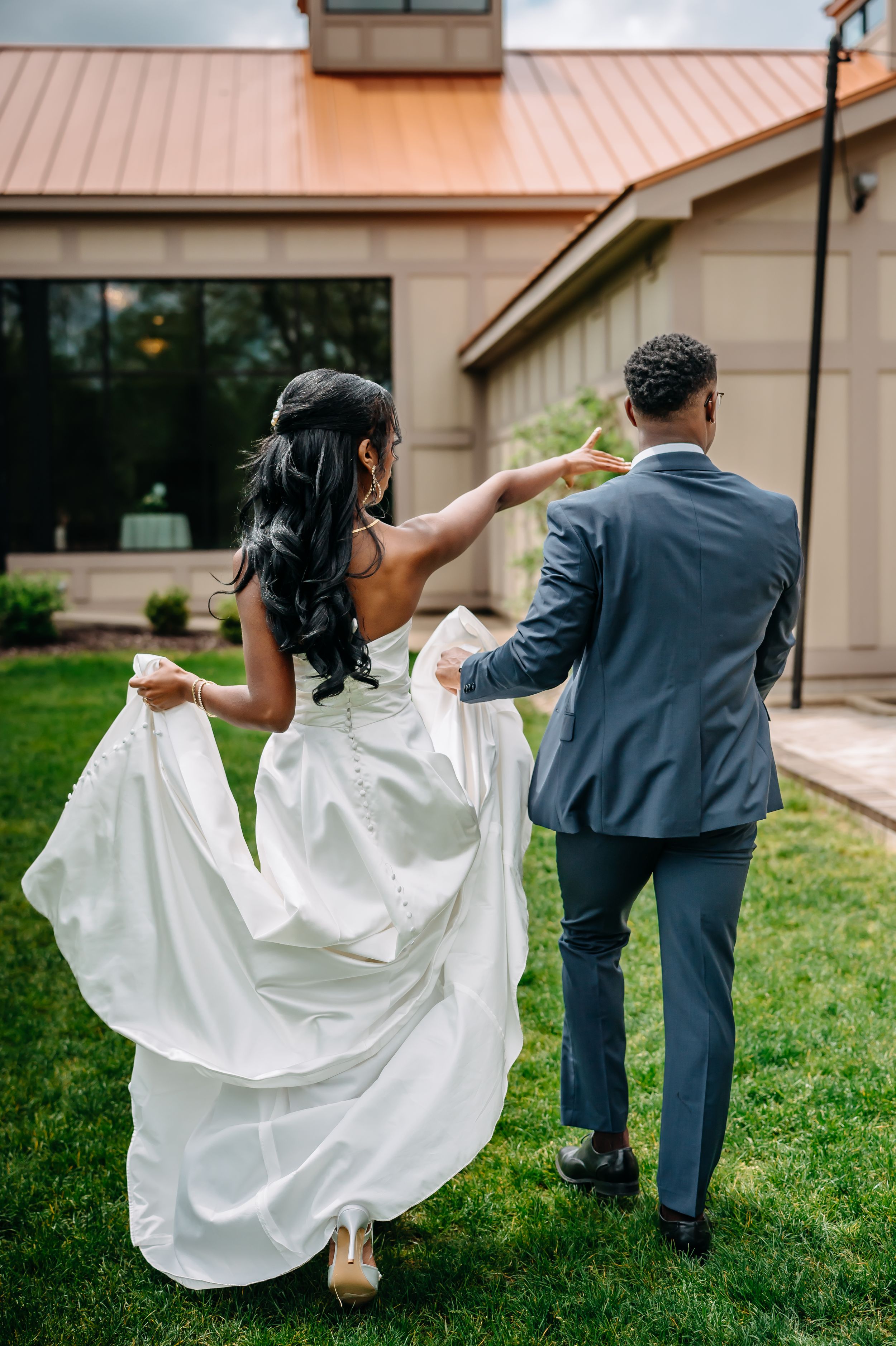 A couple dances on the lawn outside a building while the bride's white wedding dress flows in the breeze.