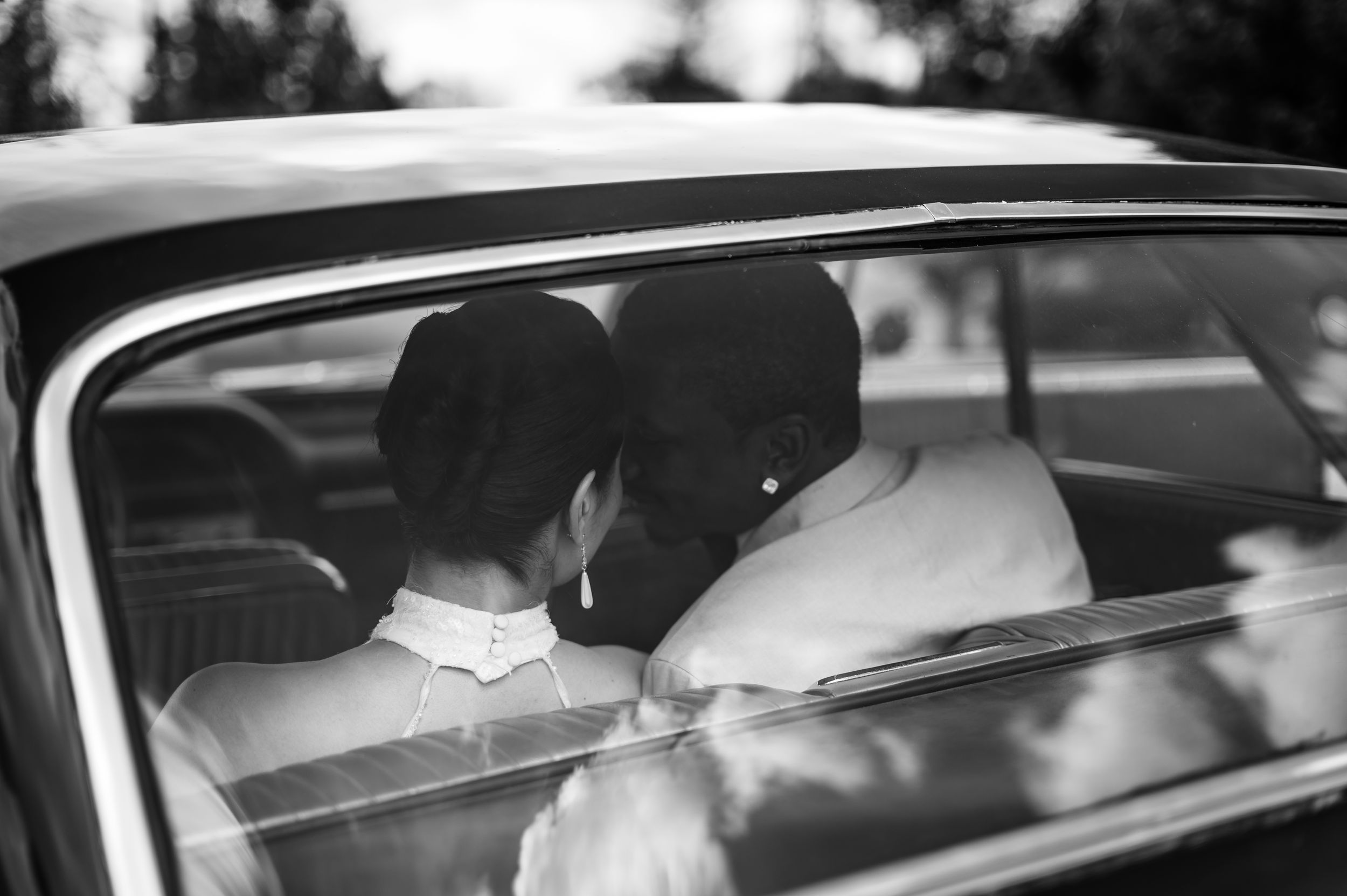 Black and white photo showing the back of a couple sitting in a vintage car, viewed through the rear window.