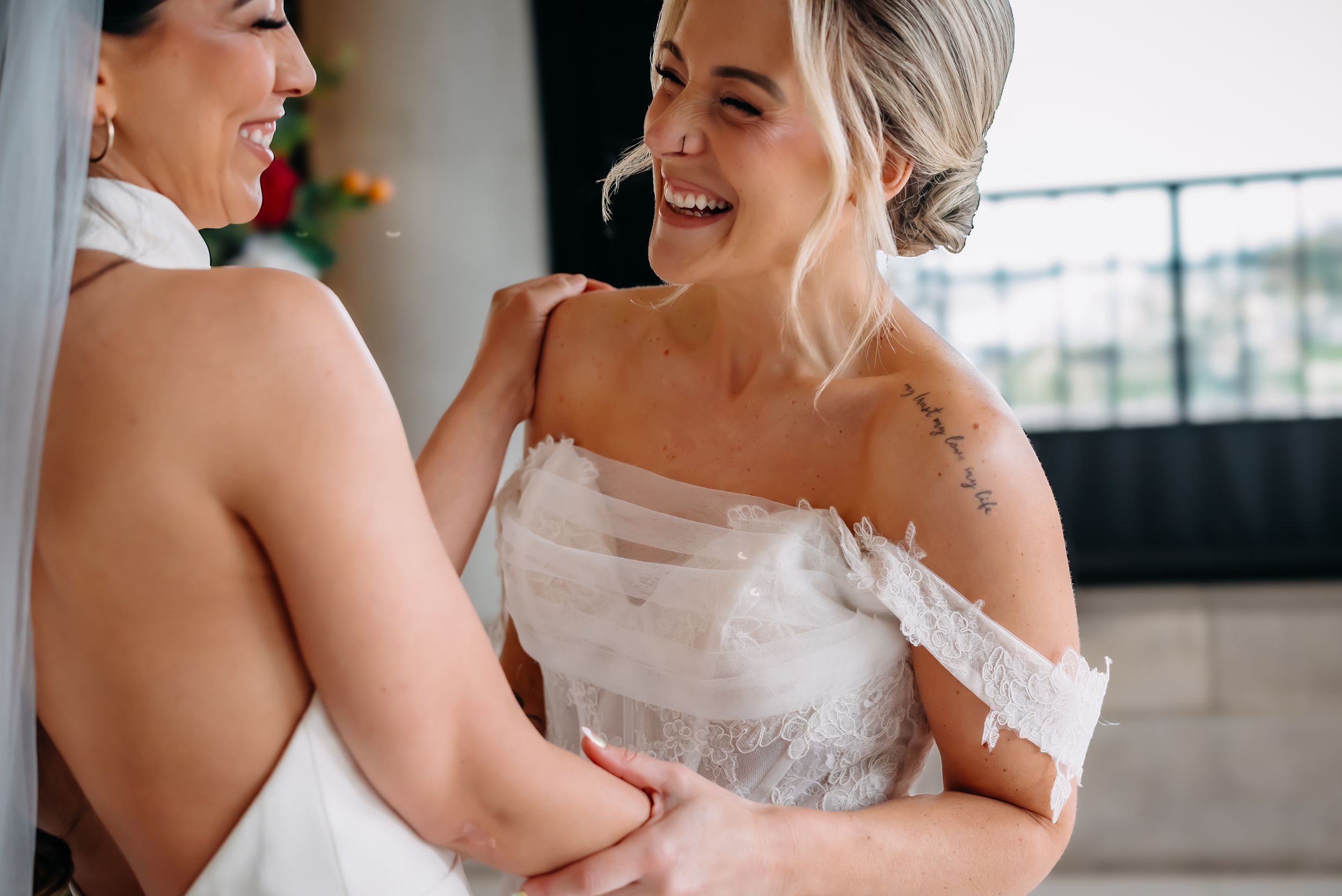 Two individuals in elegant white wedding dresses share a joyful, intimate moment together.