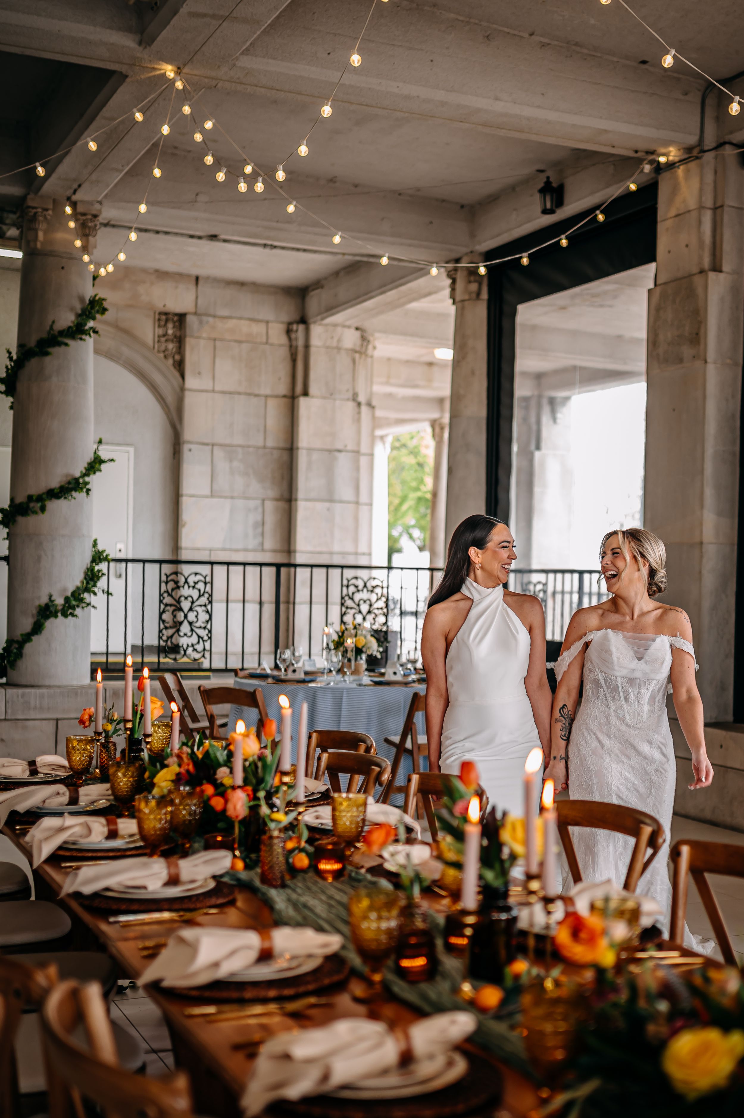 An elegant wedding reception table decorated with autumn florals and string lights in a rustic indoor venue.